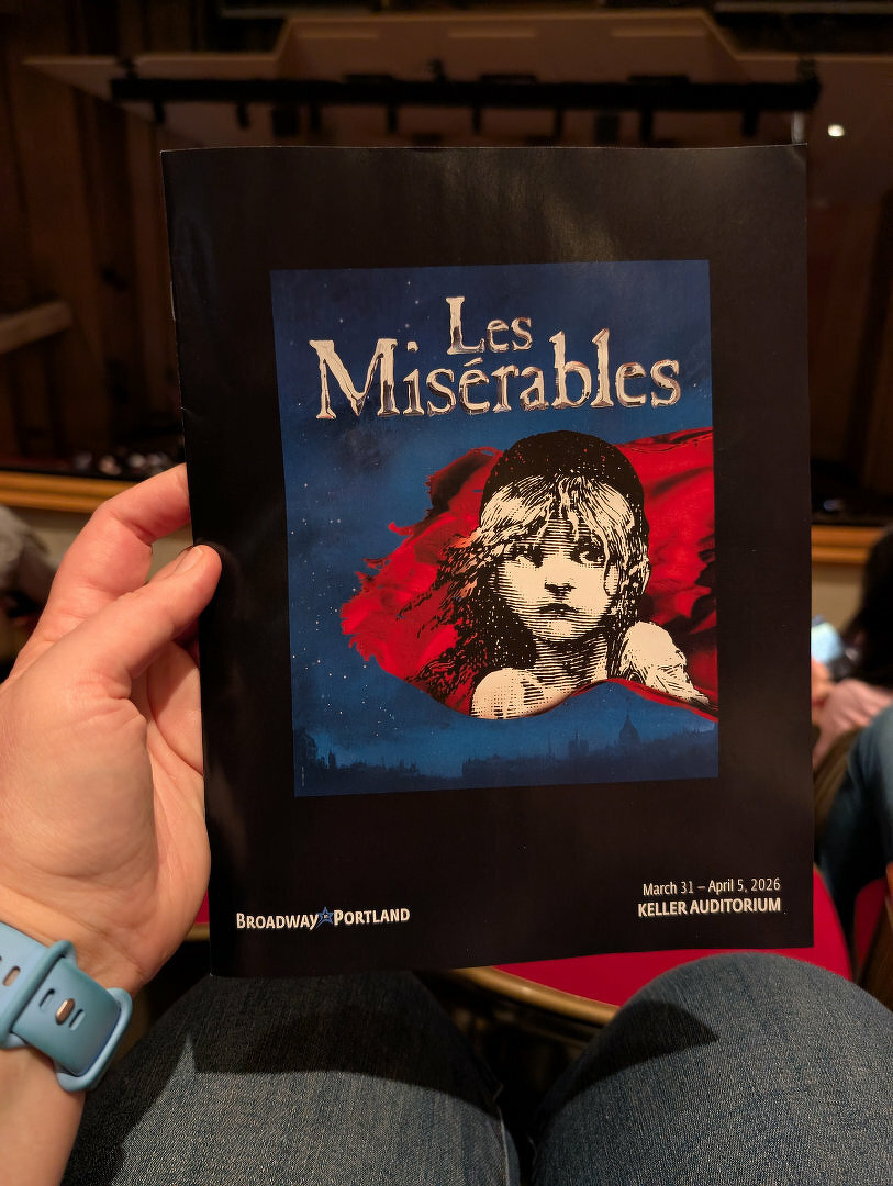 A person is holding a program for Les Misérables at the Keller Auditorium, which is scheduled for performances from March 31 to April 5, 2026.