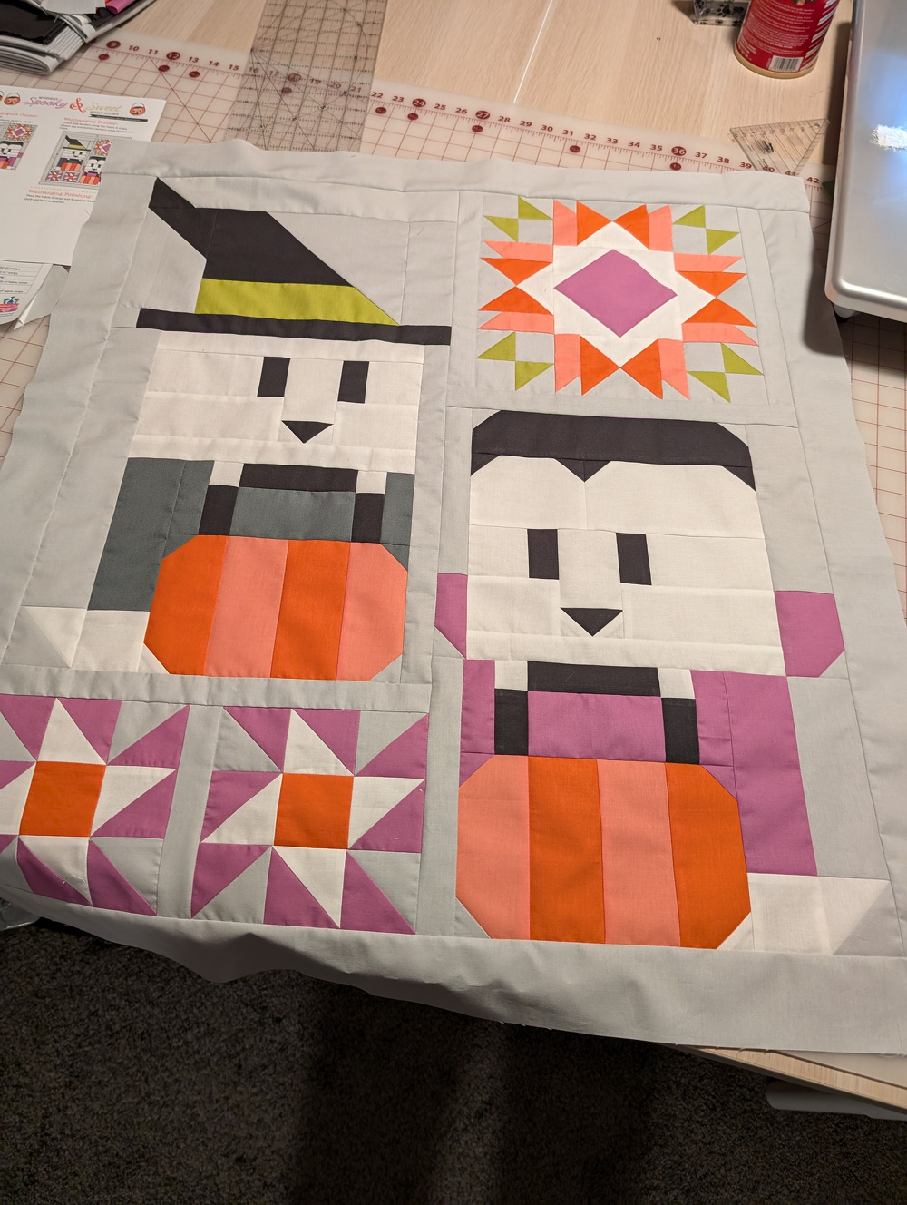 Two quilt blocks featuring abstract Halloween-themed characters, a witch and a vampire, are displayed with colorful geometric patterns.