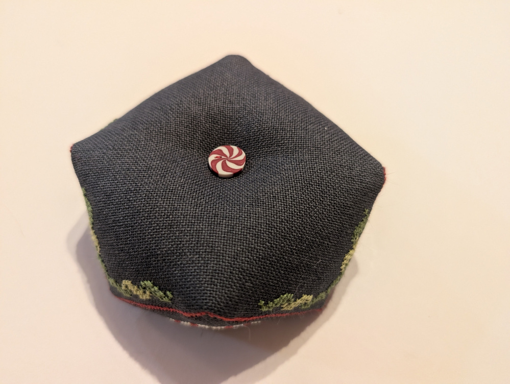 A small, fabric-stuffed cushion with a red and white peppermint swirl button on top.