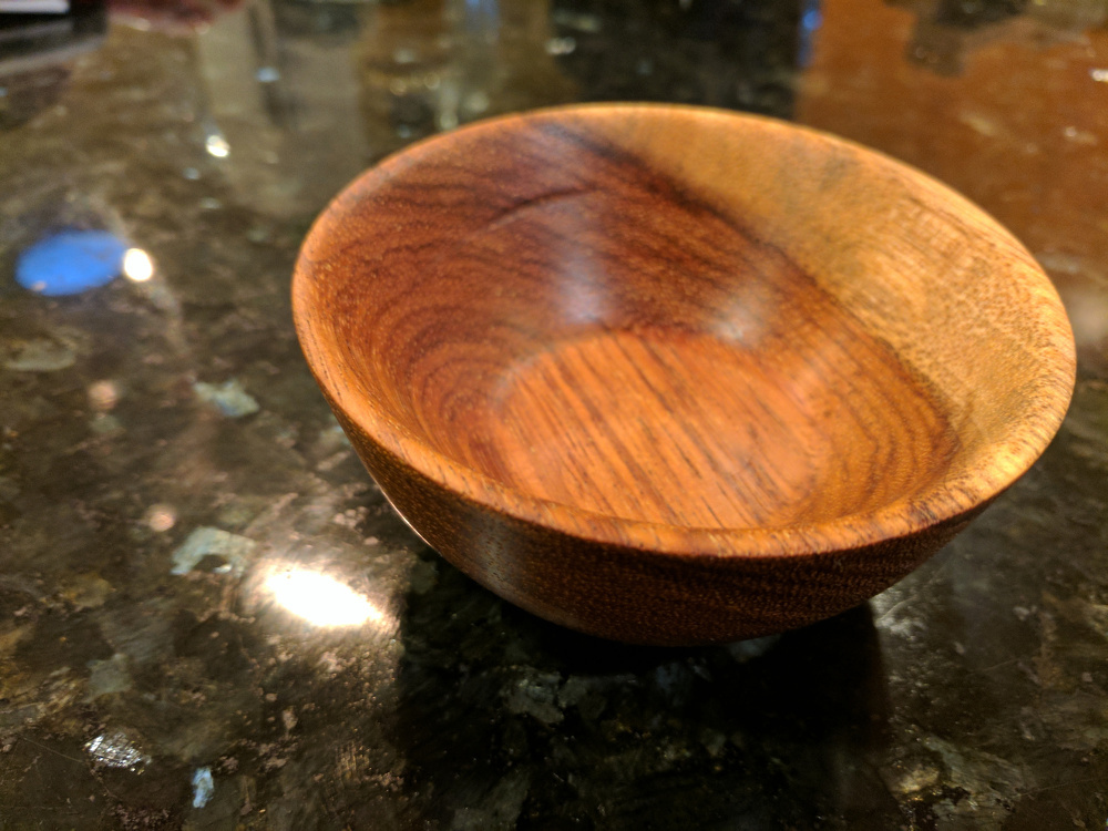 A small wooden bowl sits on a reflective dark surface.