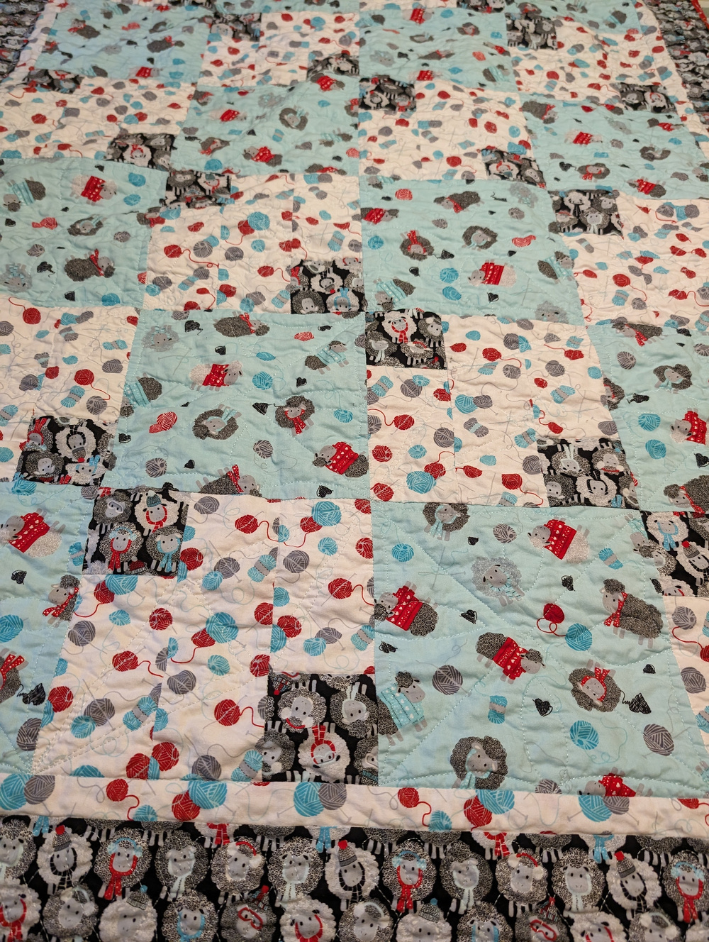A patchwork quilt features a playful pattern of elephants, polka dots, and teapots in shades of blue, red, and white.