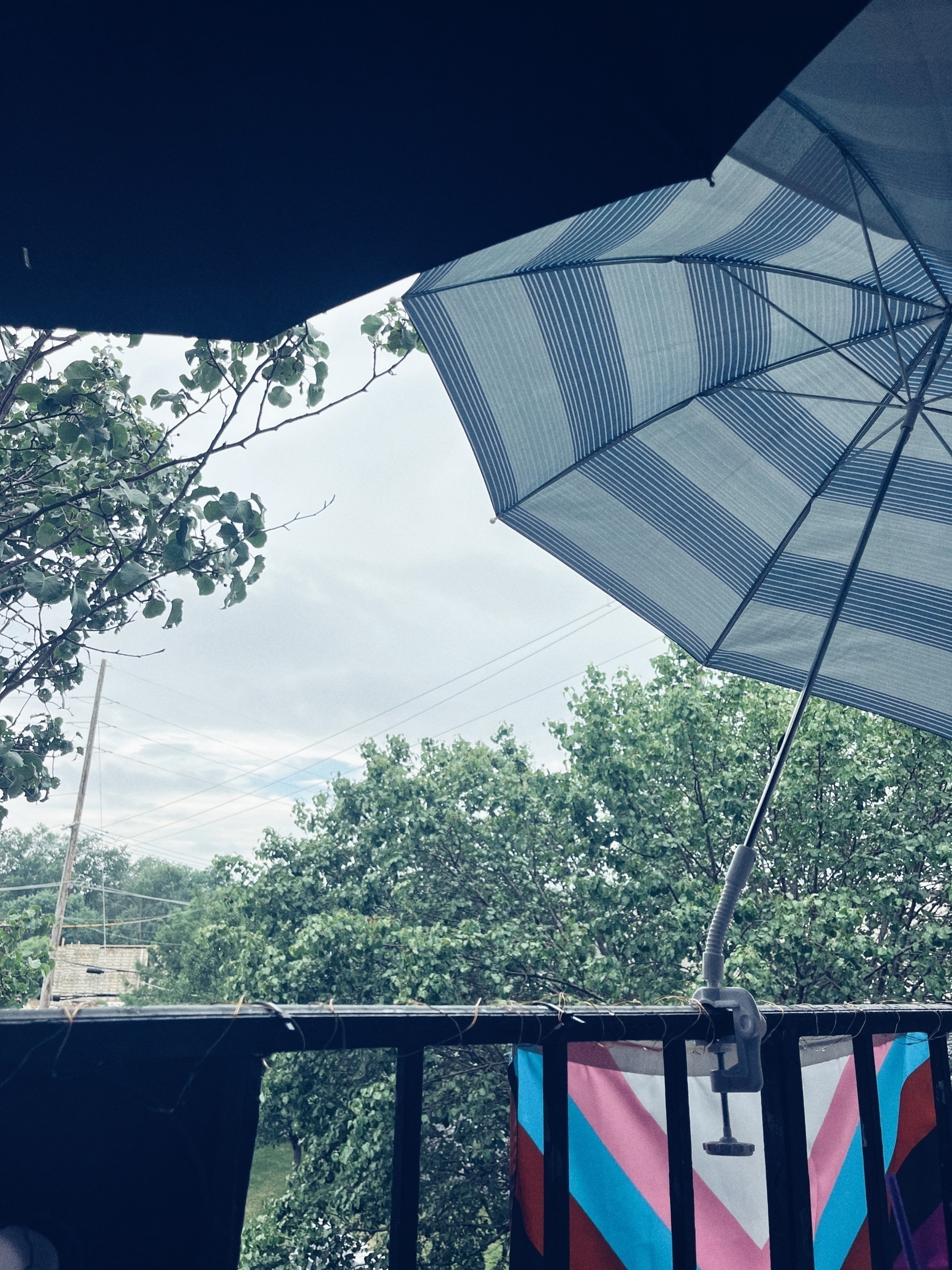 Edges of one black and one blue striped umbrella over a balcony railing with cloud sky 