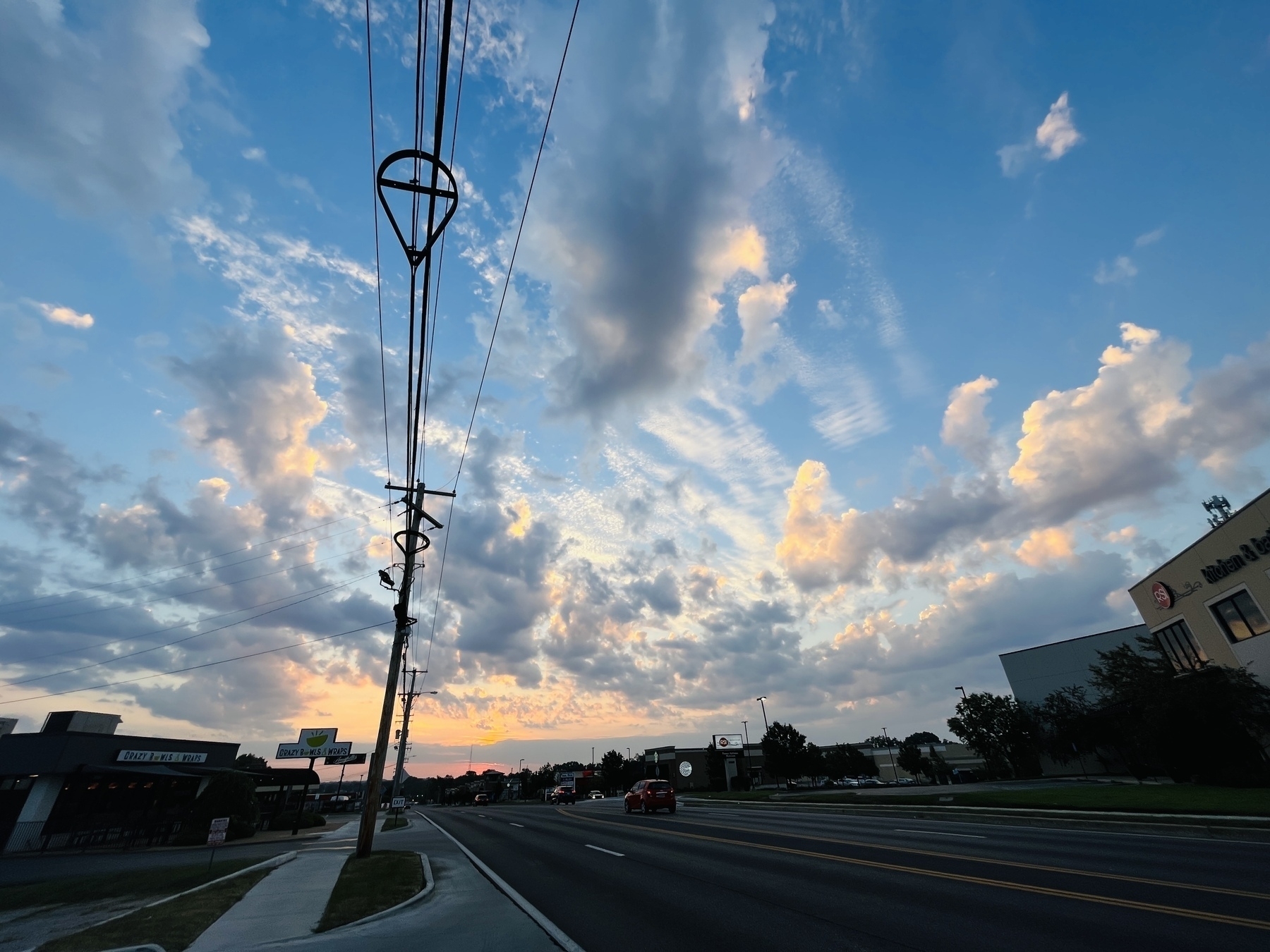 Blue skies with white clouds and orange sunrise over suburban road