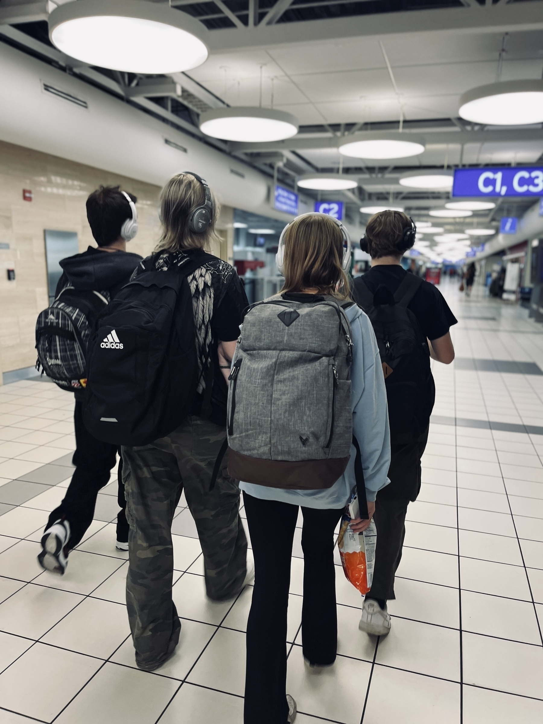 Four teenagers seen from behind walking thru an airport wearing backpacks 
