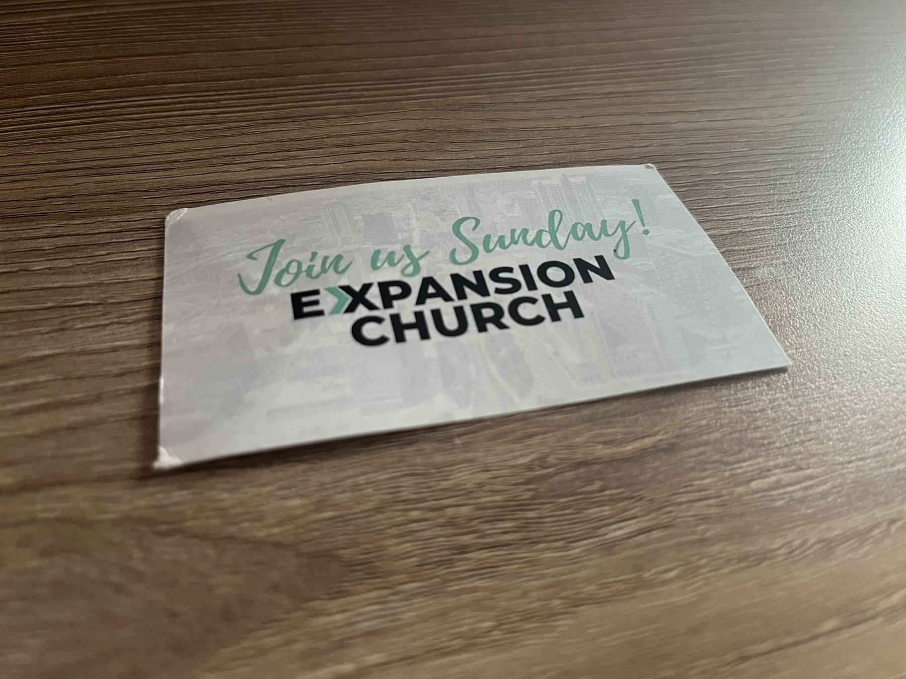 A business card that says “join us Sunday! Expansion Church” rests on a wooden table