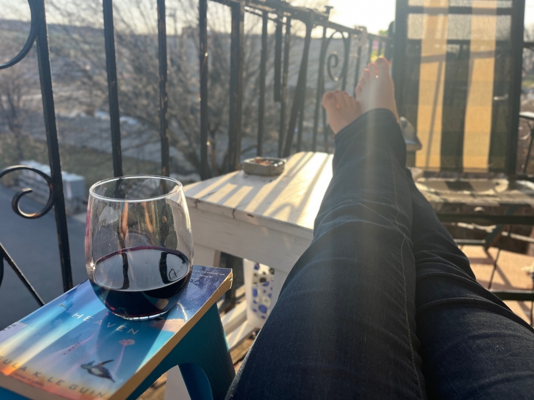 View of a glass of wine on a book and feet propped up on a balcony table 