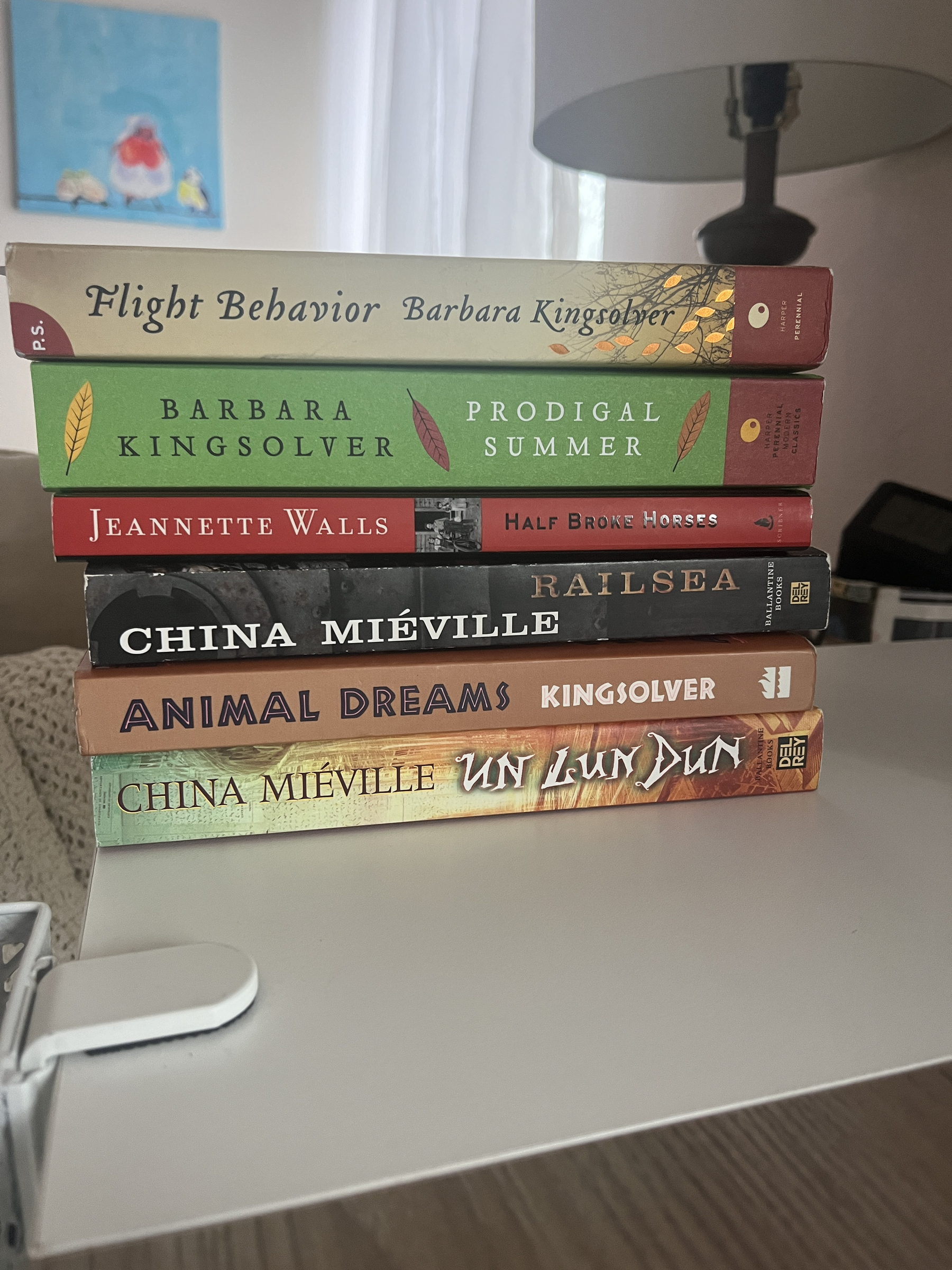 Stack of books on a desk including titles from Barbara Kingsolver, China Miéville, and Jeanette Walls