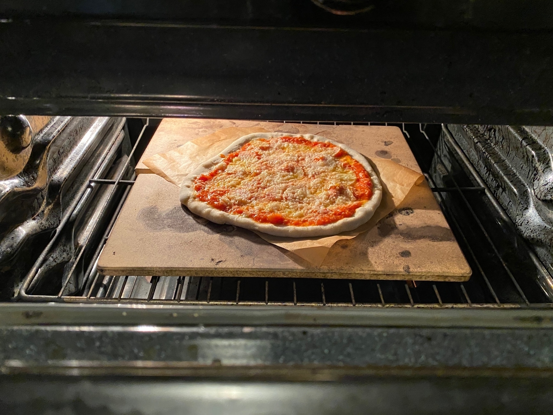 Small uncooked pizza on a baking stone in an open oven.