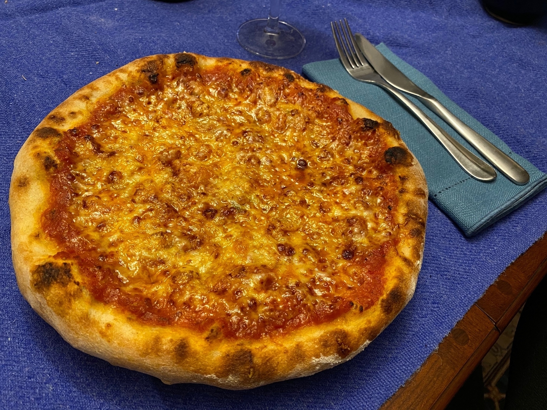 A small pizza on a plate next to a knife and fork.