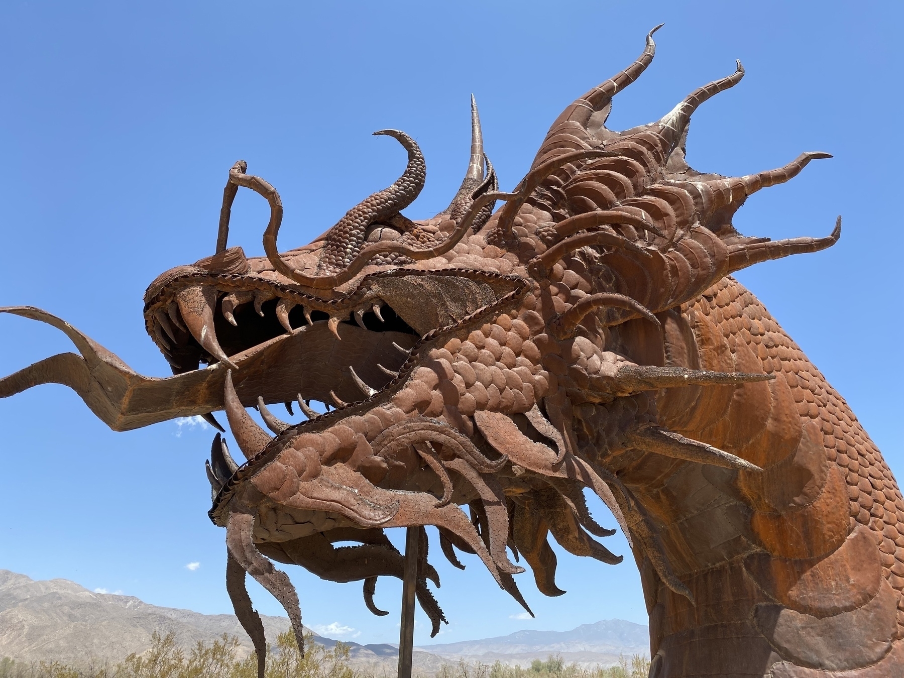 Head of a metal sculpture of a dragon against a blue sky.