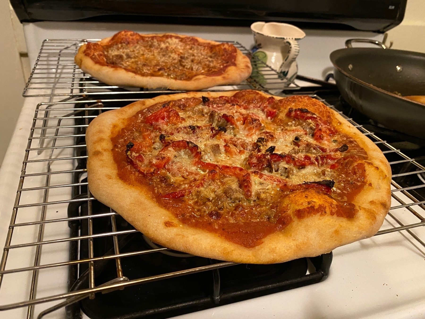 Two small pizzas on cooling racks on a stove.