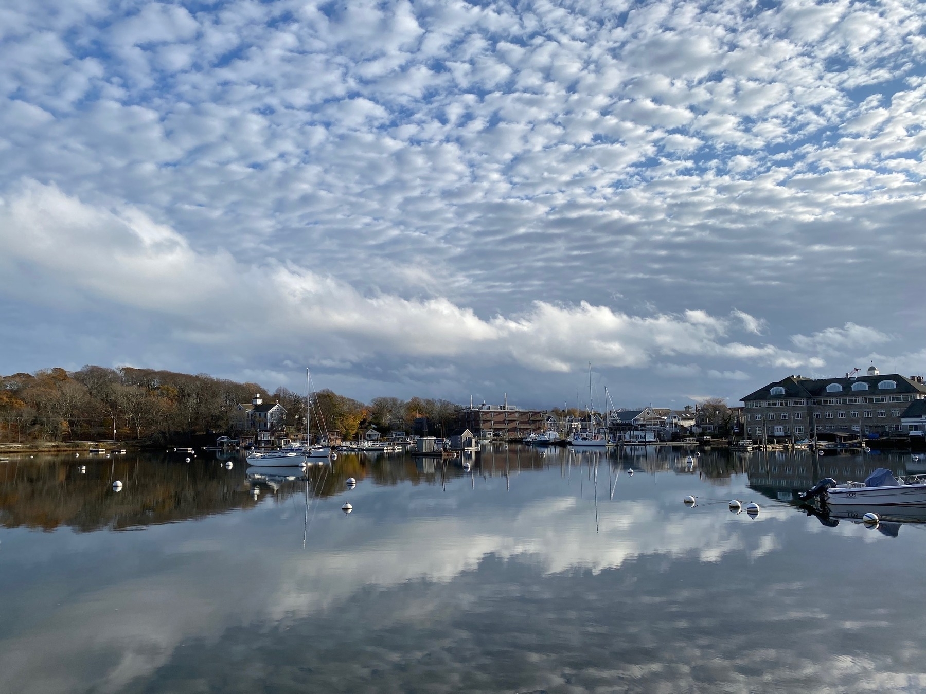 View of Woods Hole Harbor in the afternoon, with many puffy clouds dotting the blue sky above.