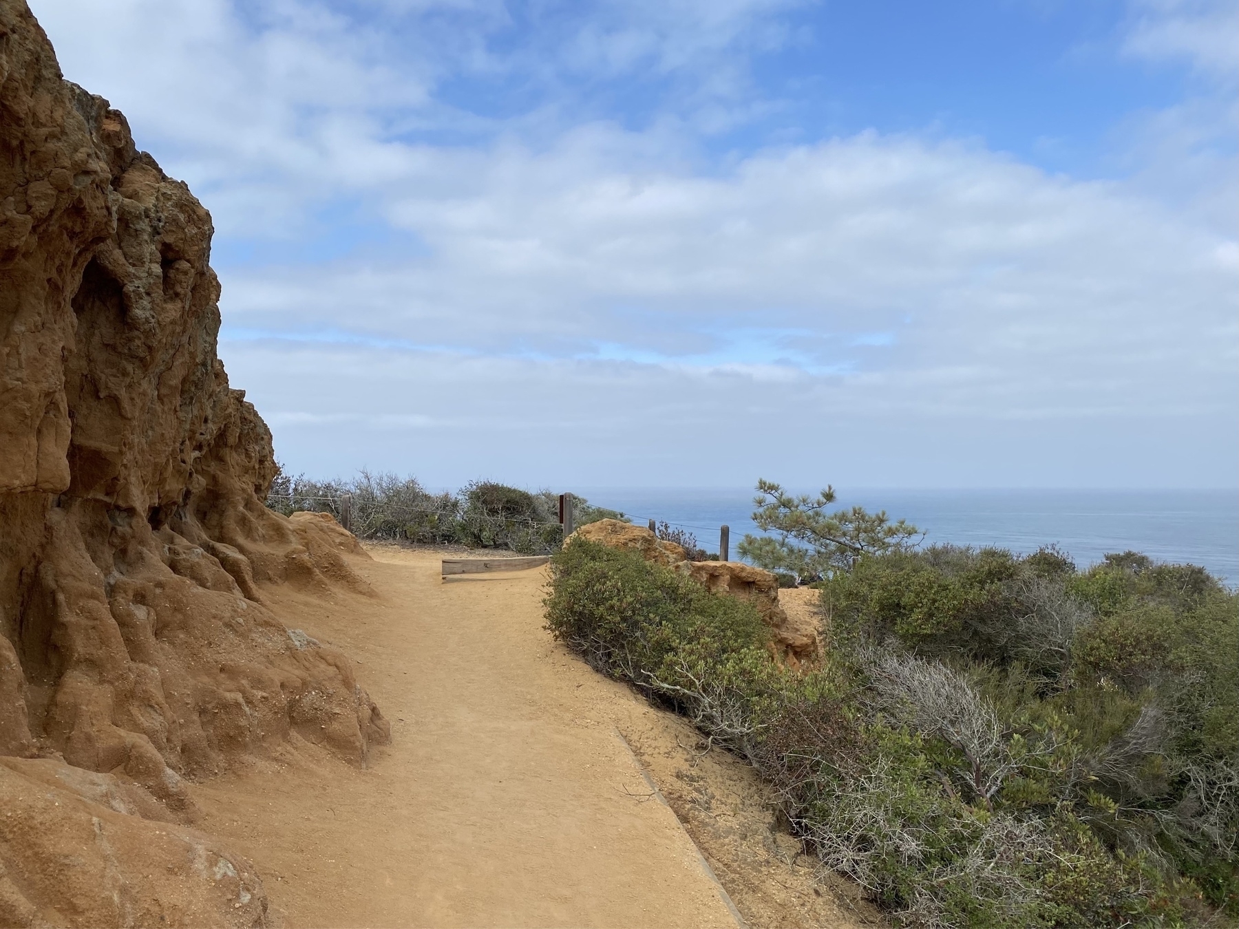 View of a dirt path leading pas an eroded cliff with the ocean in the background.