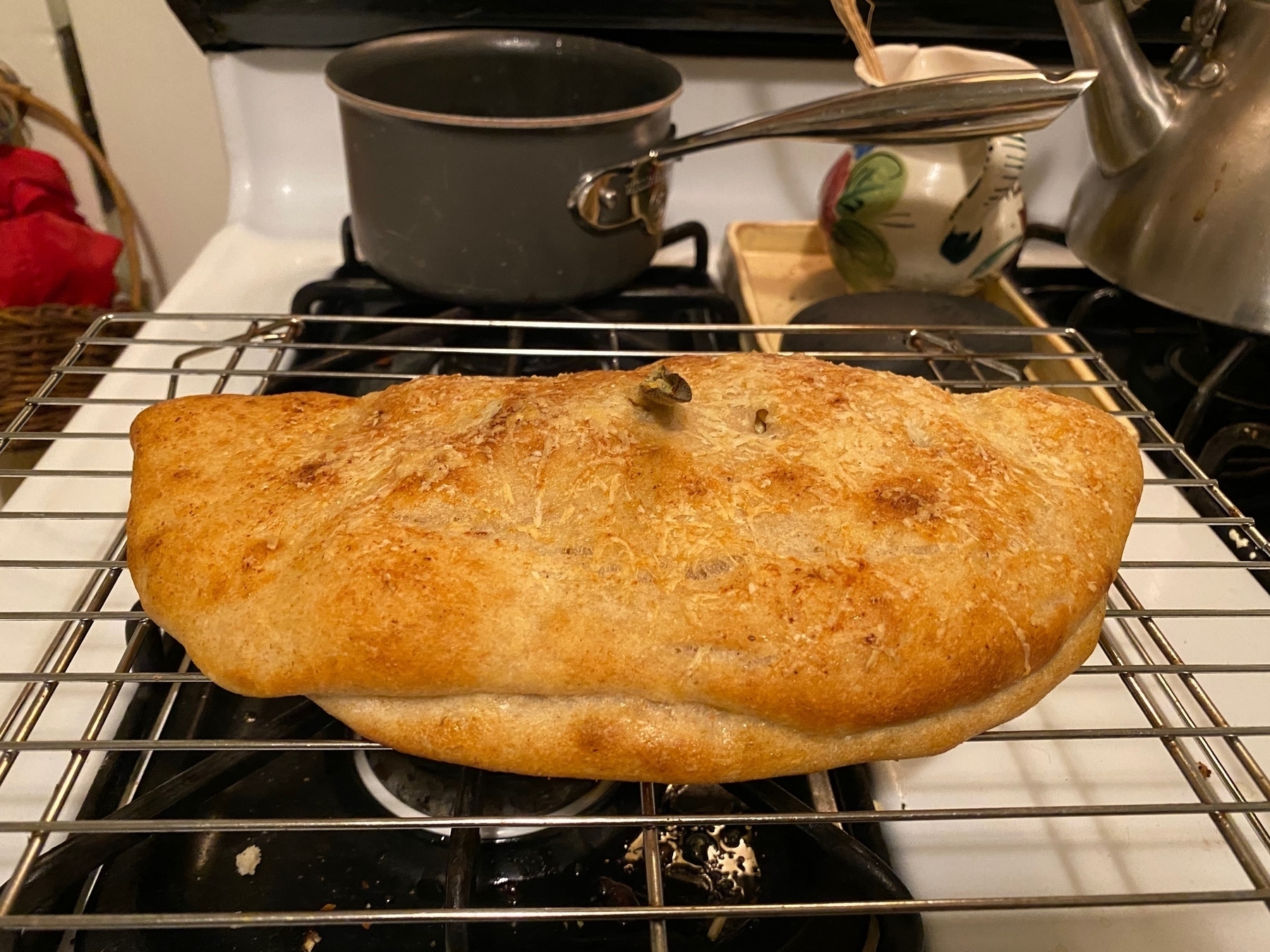 A small calzone on a cooling rack on top of a stove.