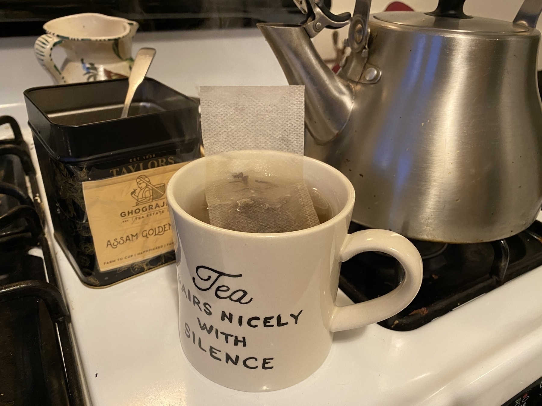 Close up of a cup of tea steeping on a stove, with a kettle and tea box in the background.