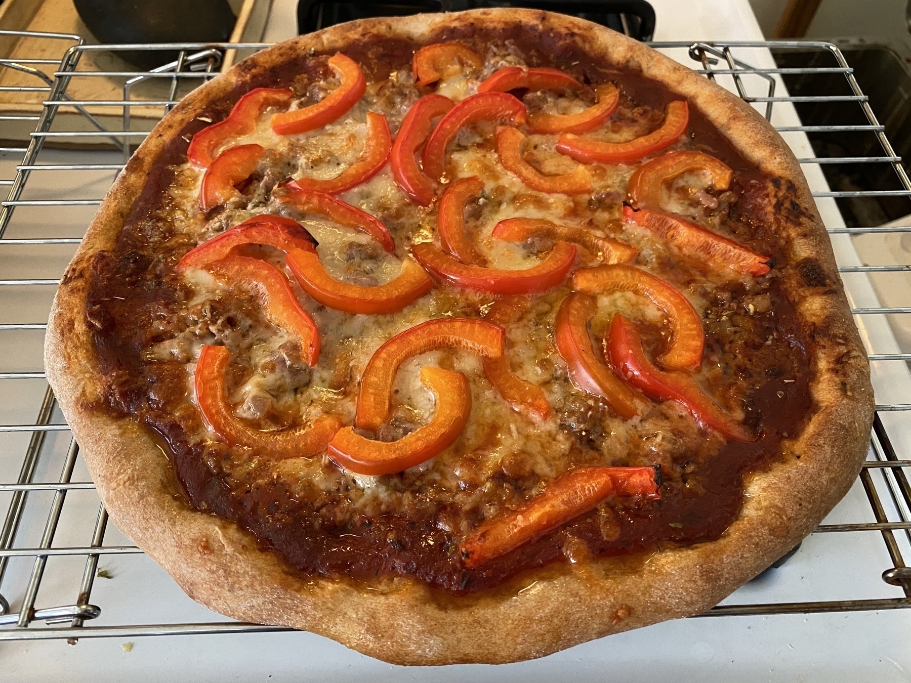 Small pizza on a cooling rack covered in slices of red bell pepper.