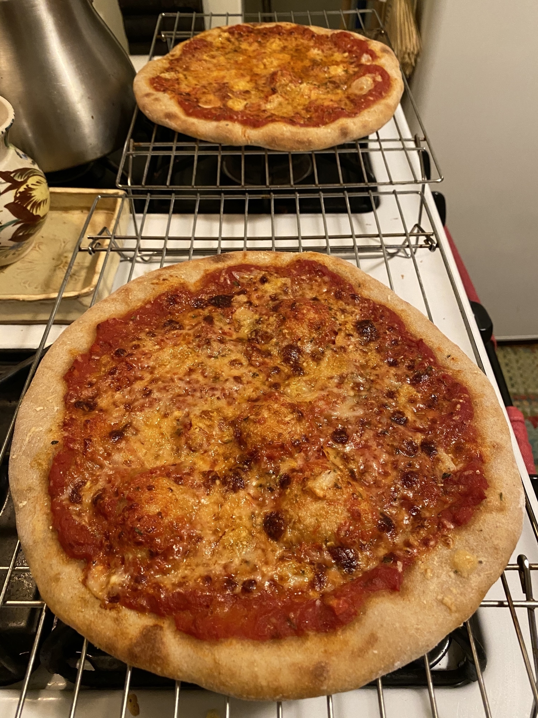 Two small pizzas on cooling racks on a stove.