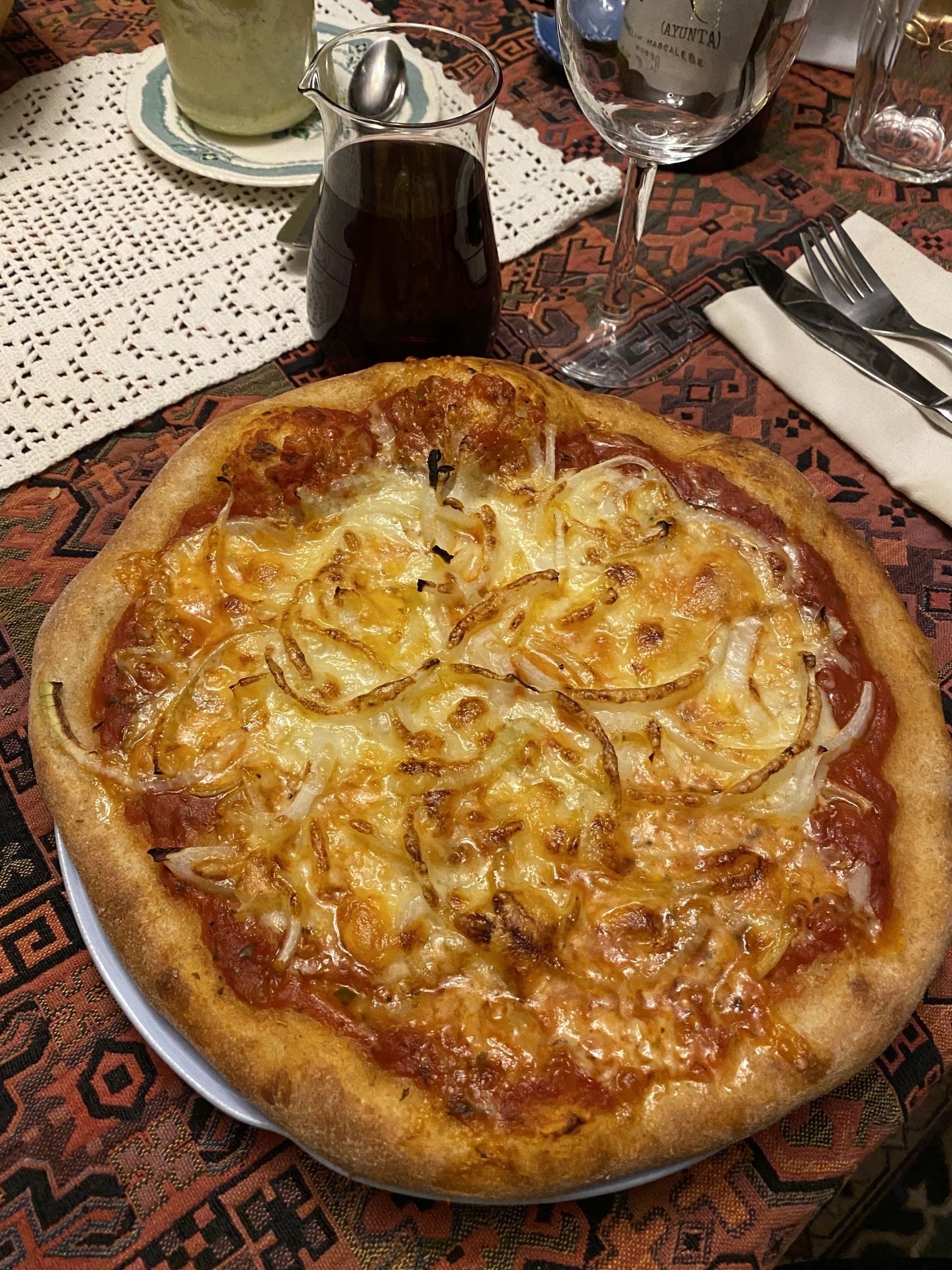 Small pizza on a plate next to a glass of wine.