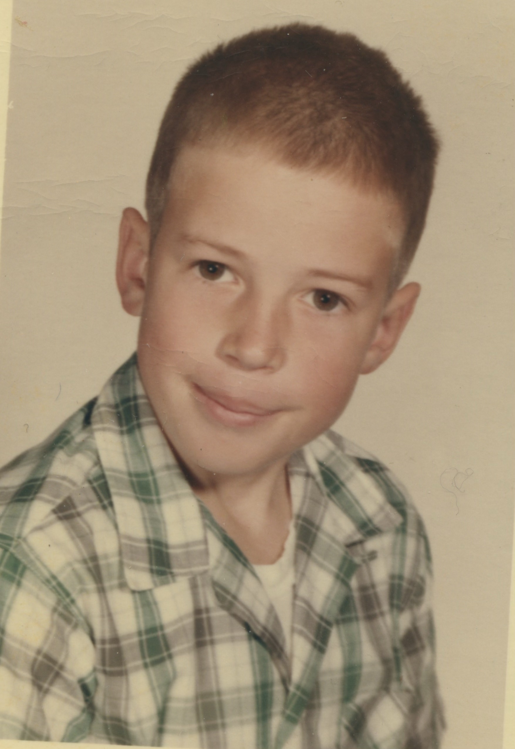 Portrait of a young boy with short hair wearing a green plaid shirt.