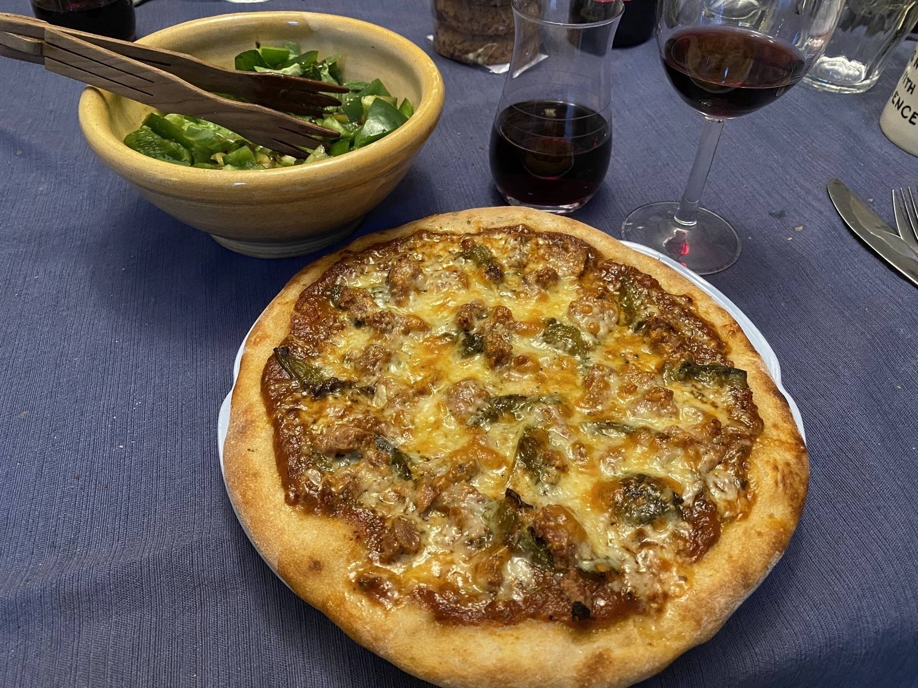 Small pizza on a plate, next to a small bowl of salad and a glass of wine.