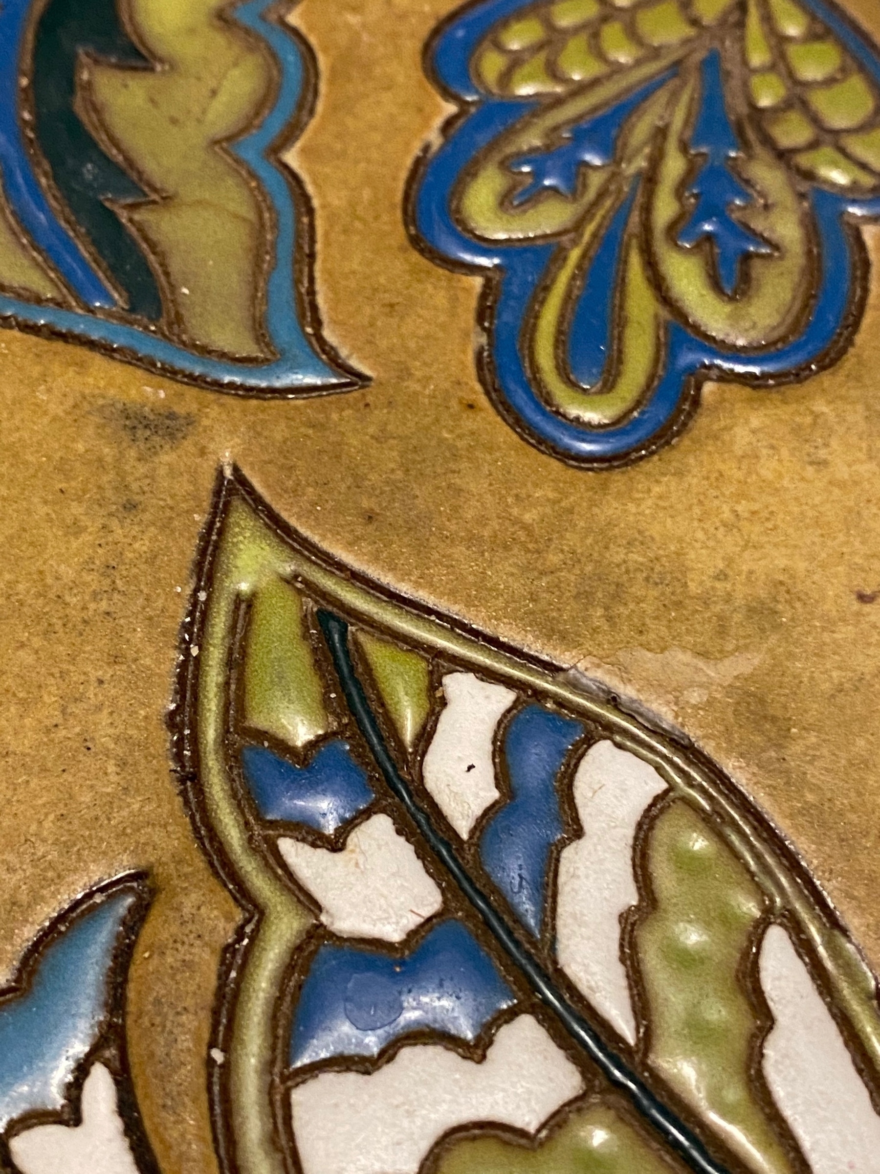 Close up of a ceramic tile with blue, green, and yellow leaf shaped decorations.