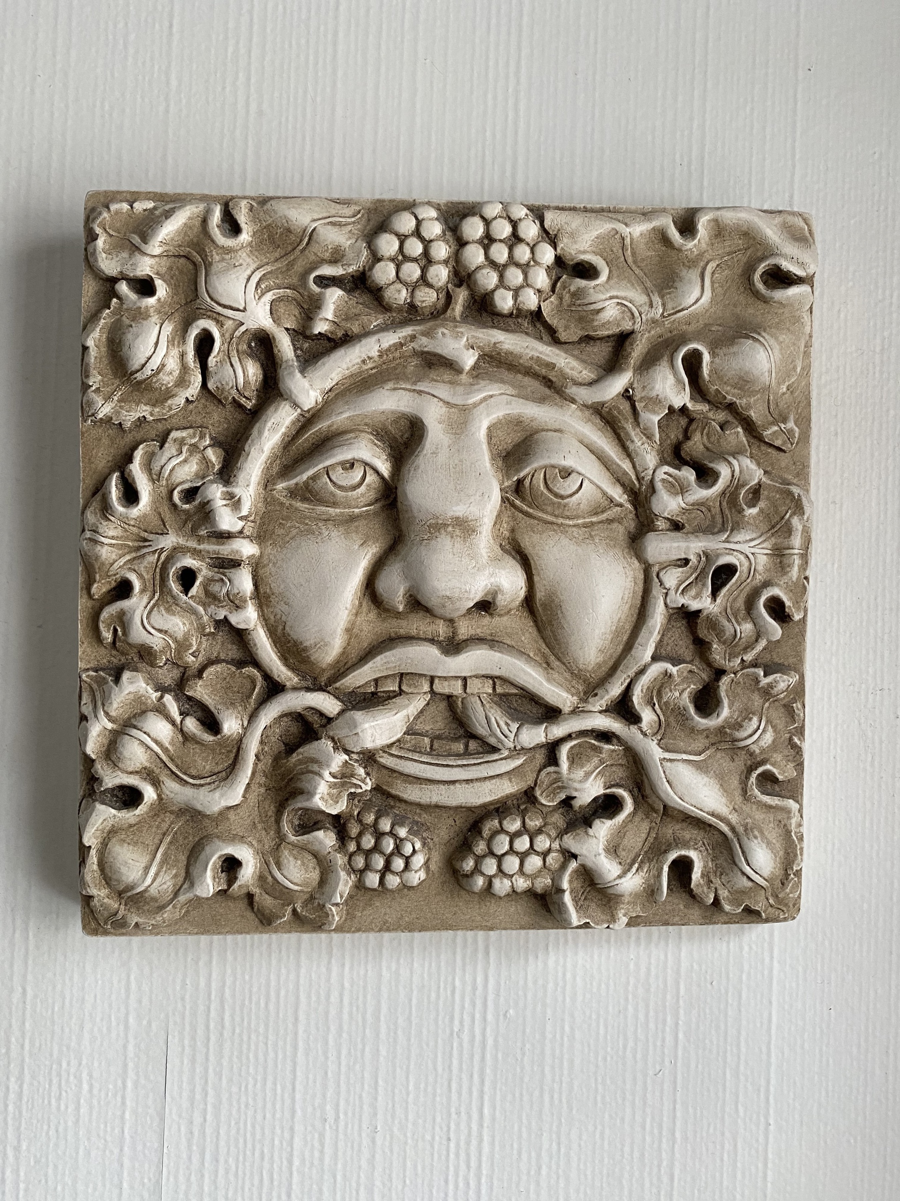 Close up of a green man tile hanging on a wall.