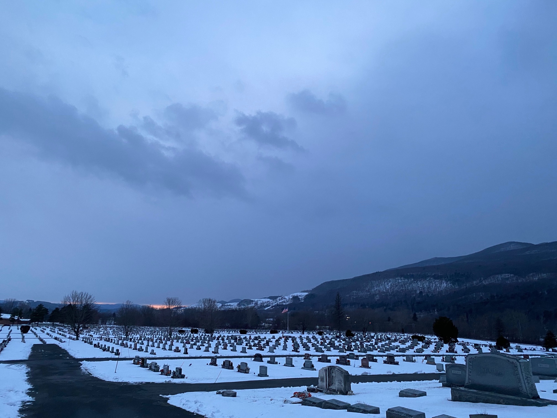 View of a snow covered cemetary, with tombstones all in rows and a cloudy gray sky above.