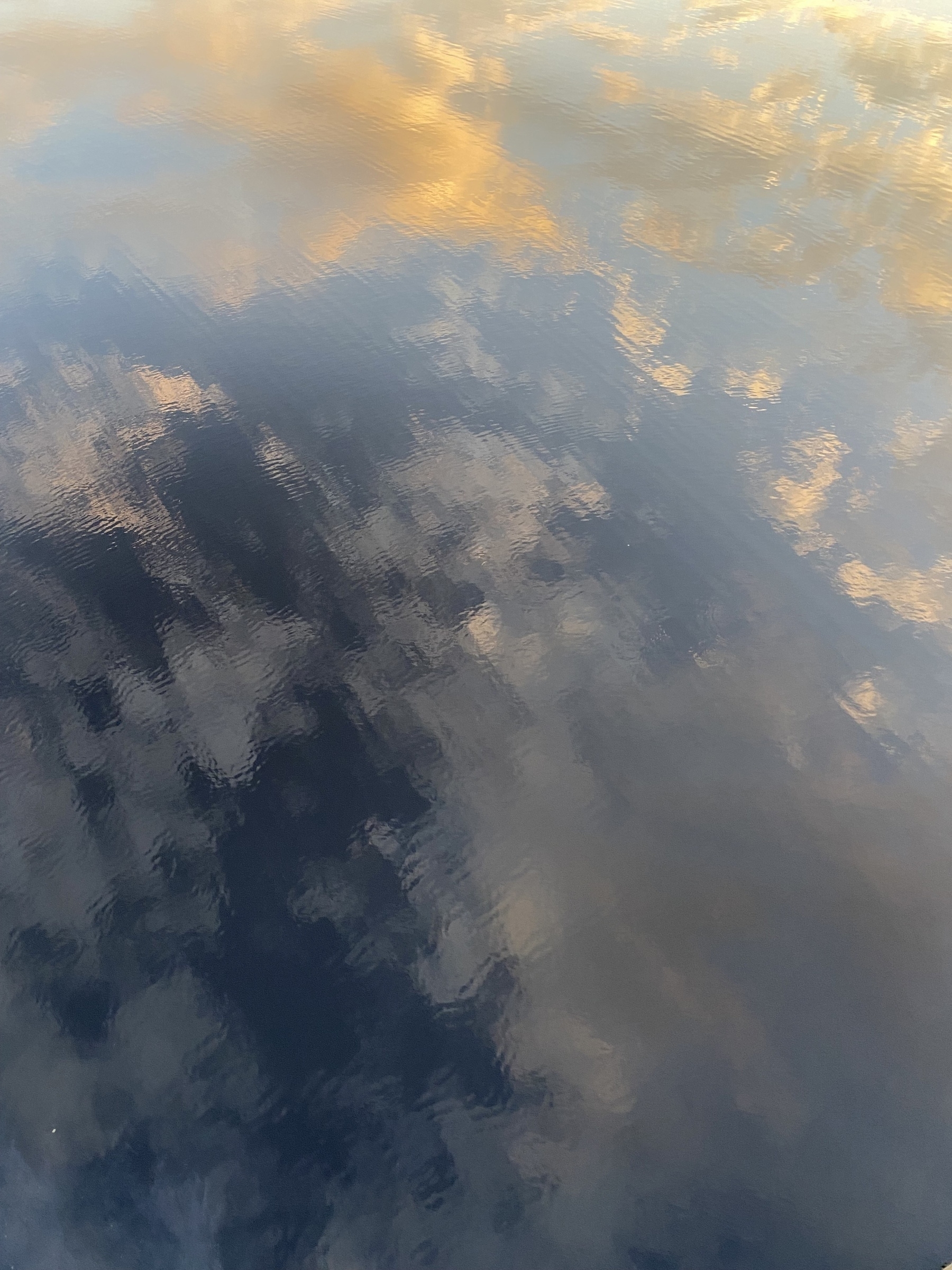 Sunset clouds reflected in rippled water.