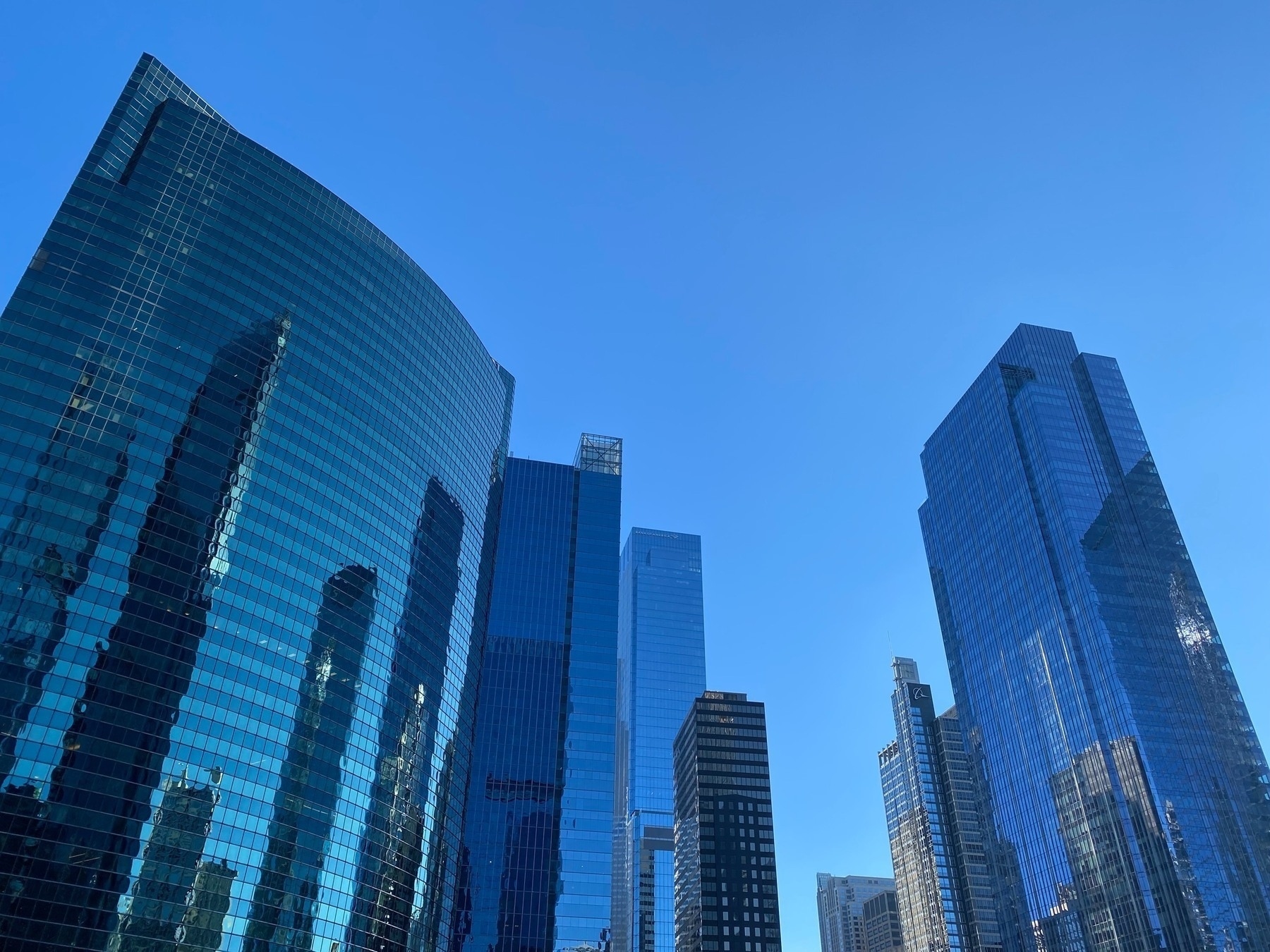 View of glass walled skyscrapers reaching into a blue sky and reflecting images of each other.