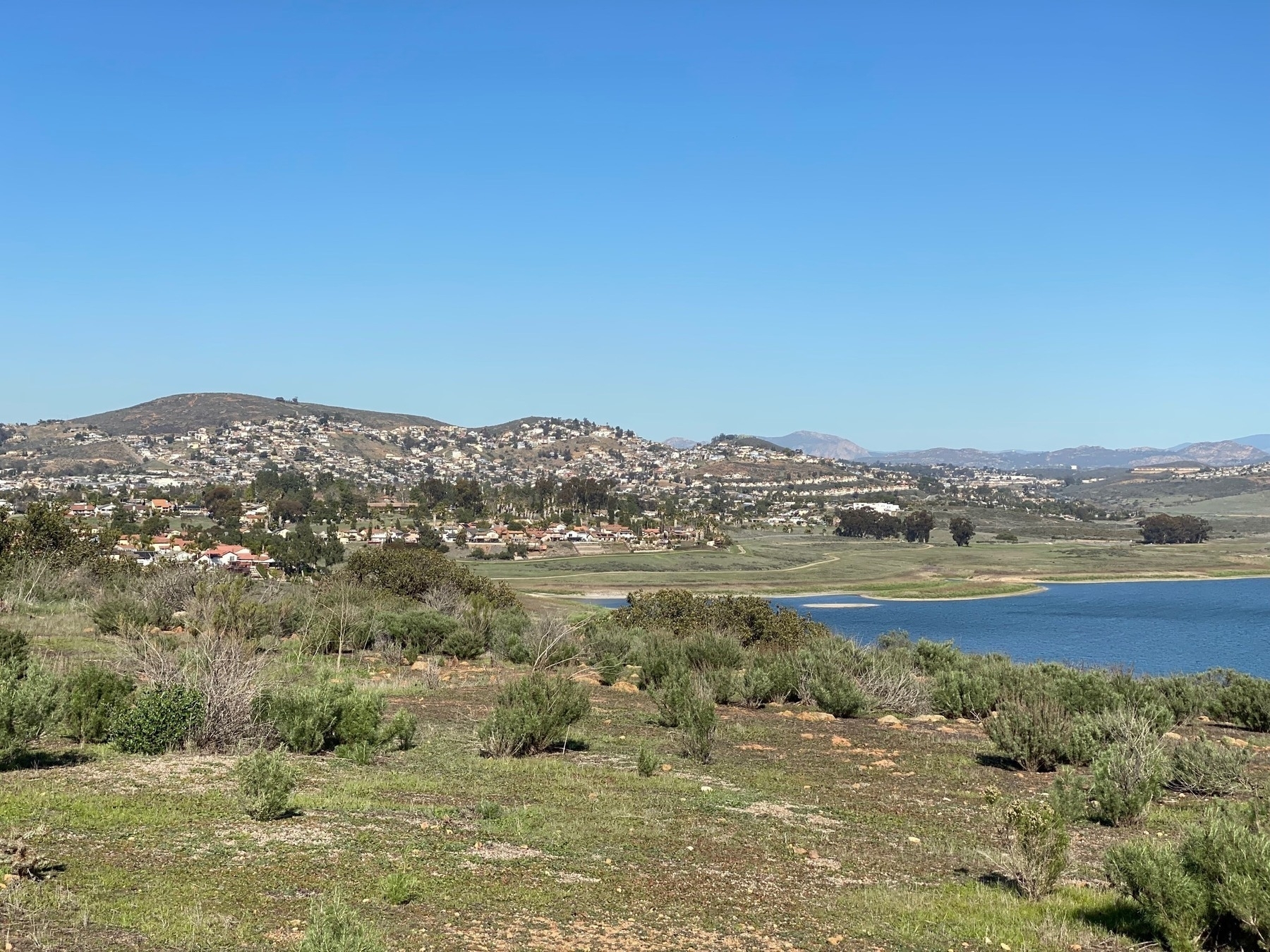 View of a reservoir surrounded by scrub brush, with houses dotting the hills on the far side.