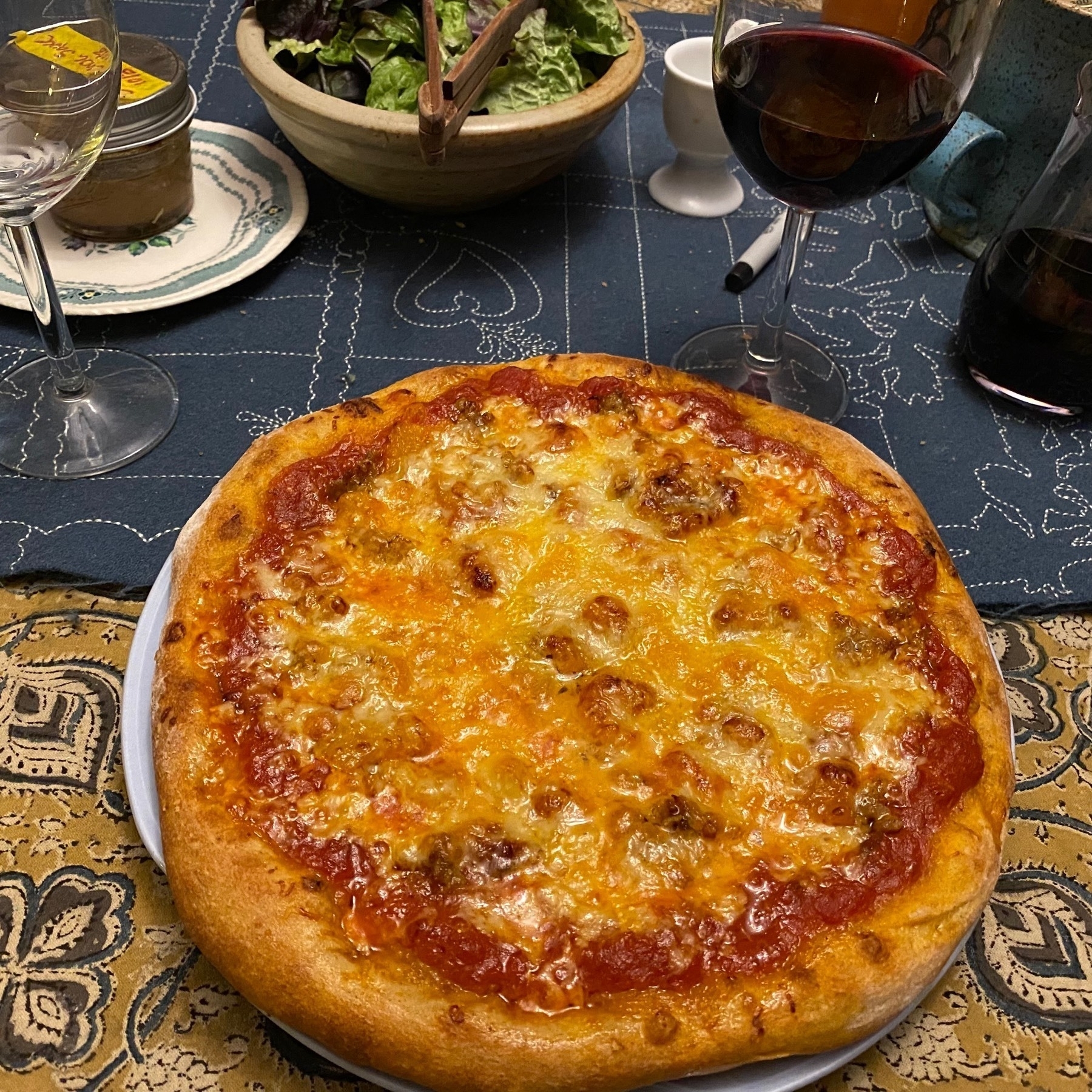 Small pizza on a table next to a salad and wine glass.