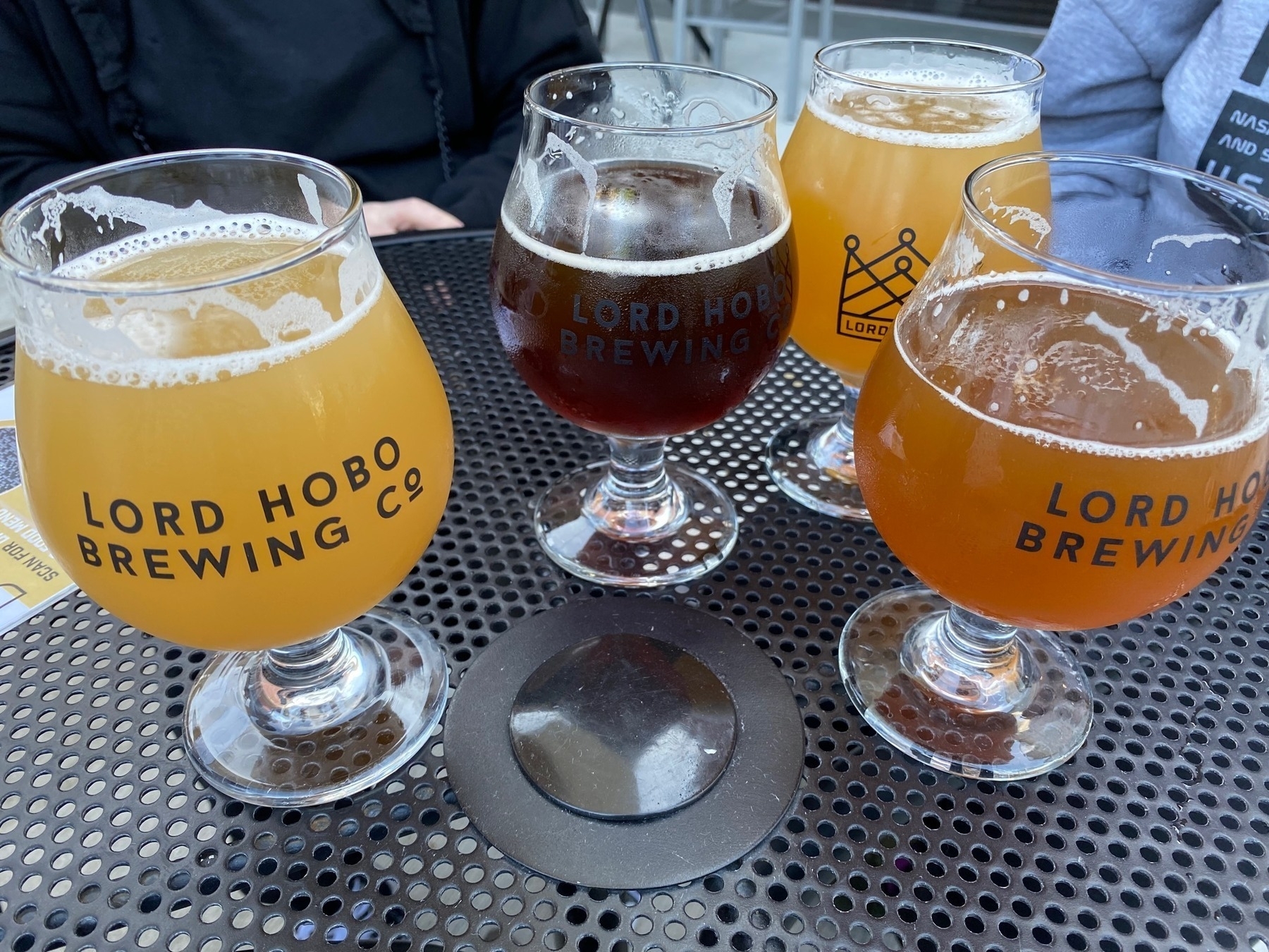 Four glasses of Lord Hobo beer on a metal table.
