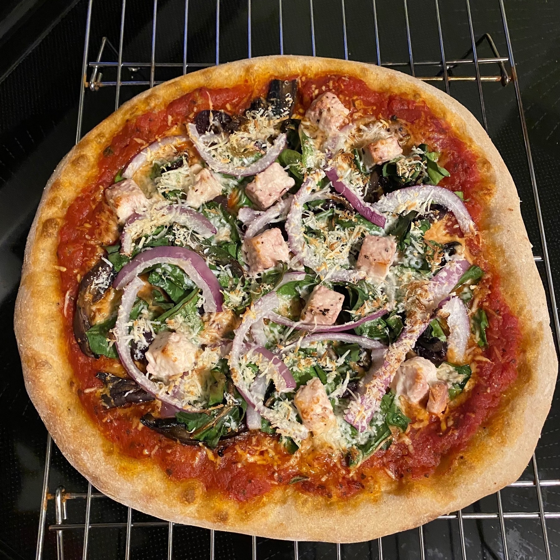 Small pizza with red onions and greens on a cooling rack.