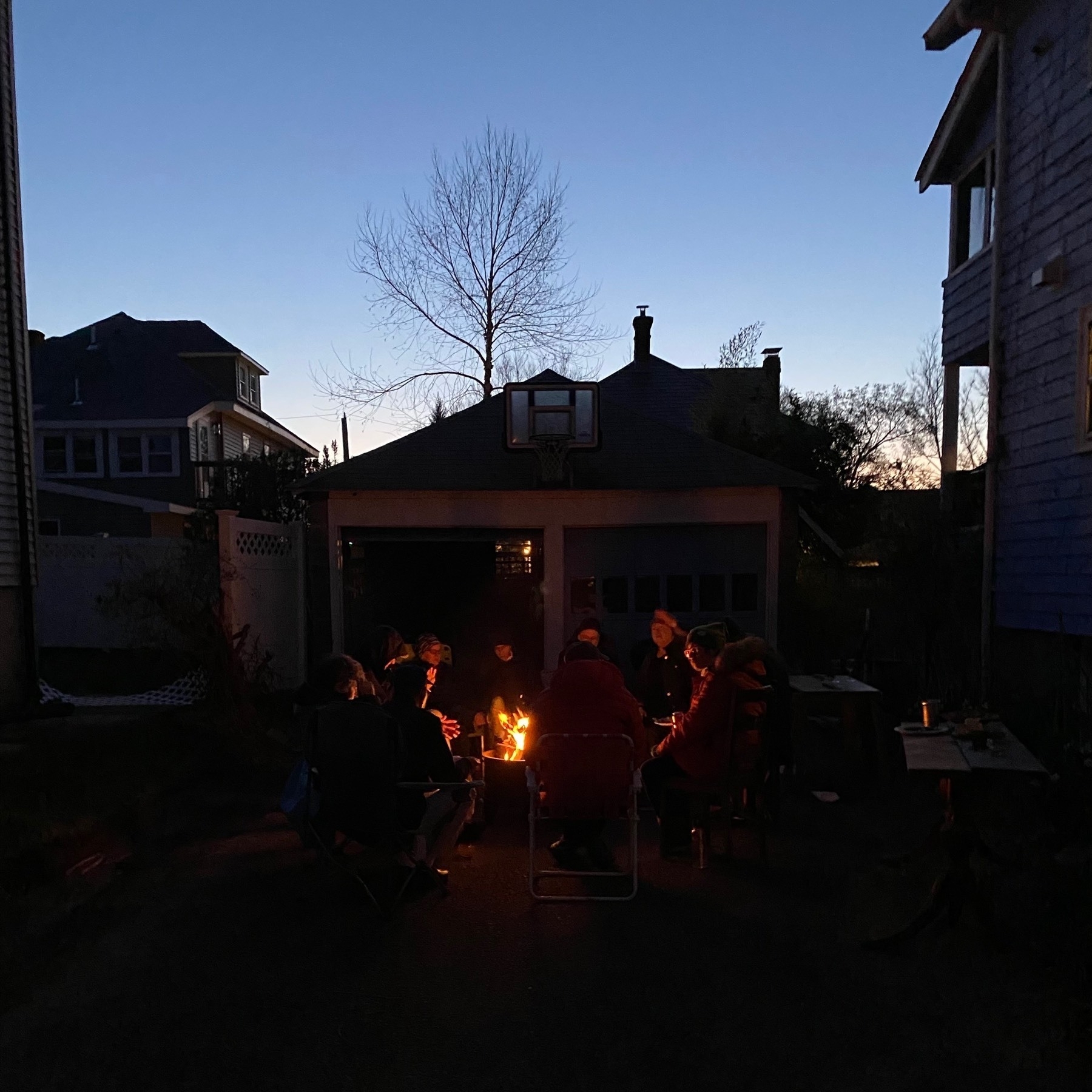 Evening view of people around a small fire with the pale blue sky in the background.