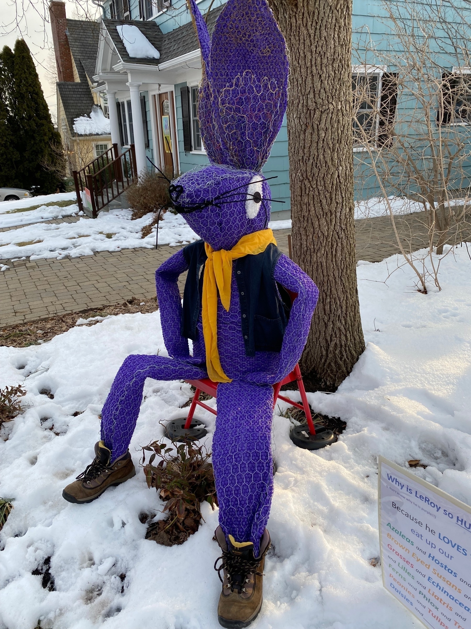 A cloth sculpture in the shape of a purple rabbit, wearing a vest, scarf, and boots.
