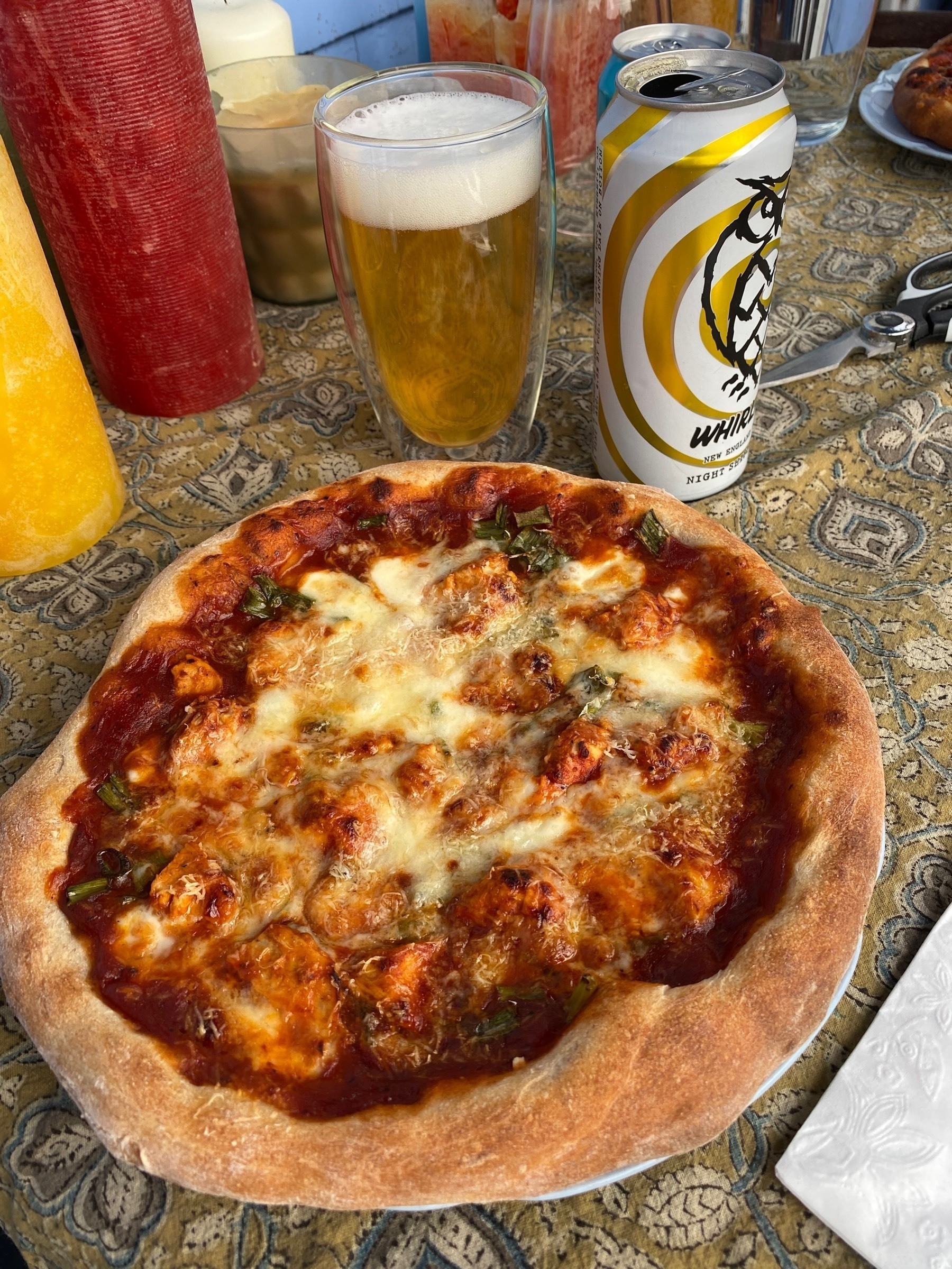 Small pizza on a table next to a glass of Whilpool beer.