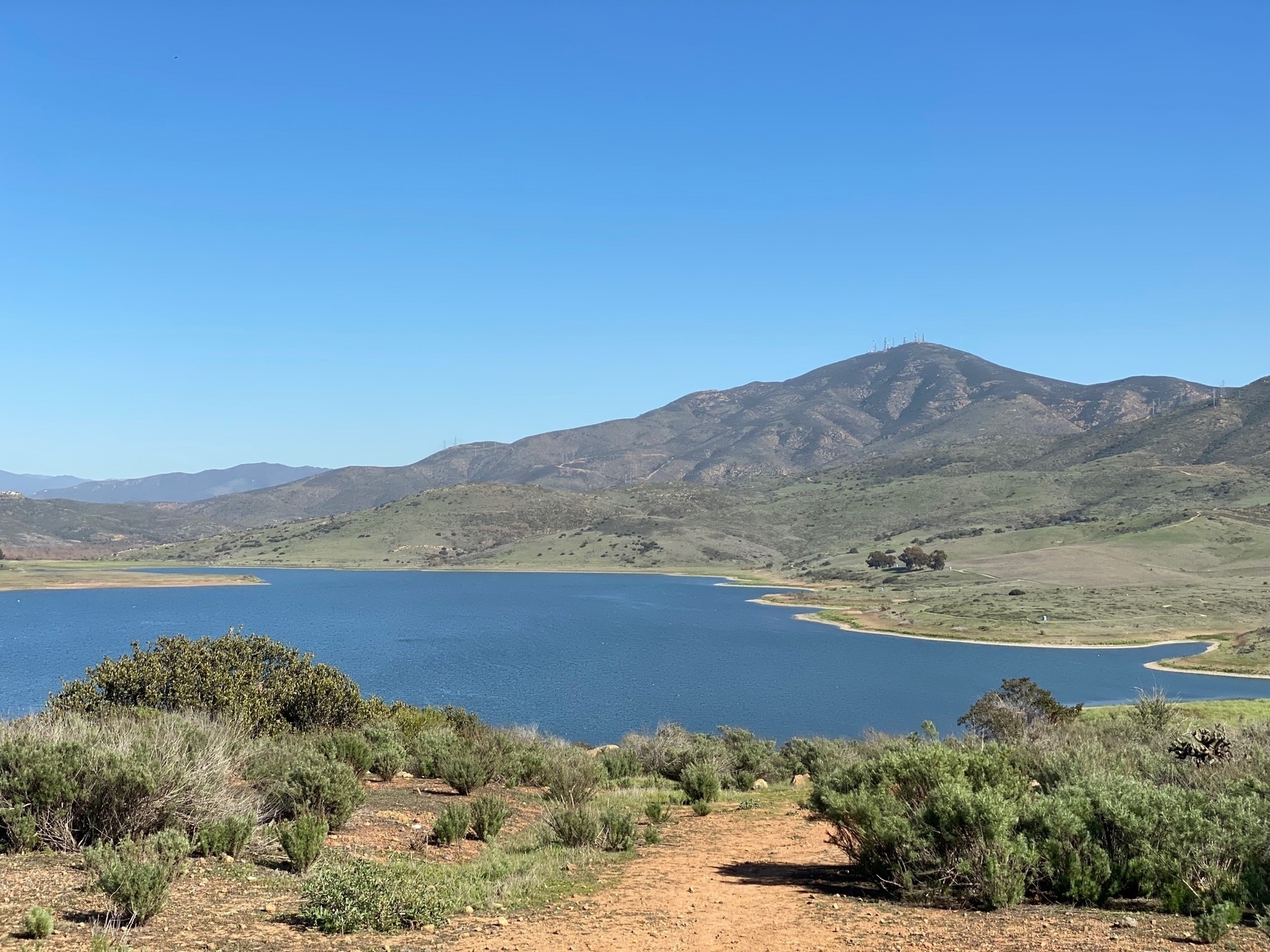 View of a reservoir surrounded by scrub brush, with a tall mountain on the far side.