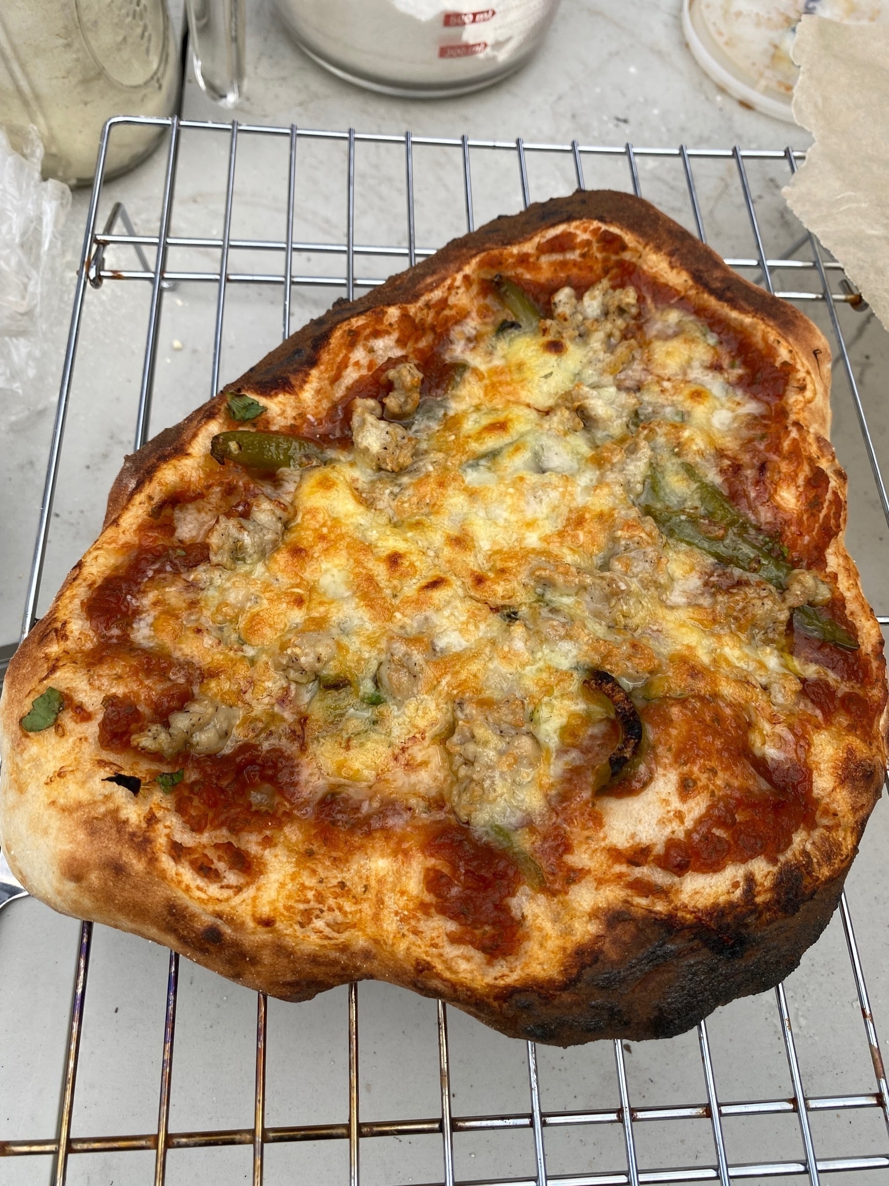 A small pizza on a cooling rack, not quite round.