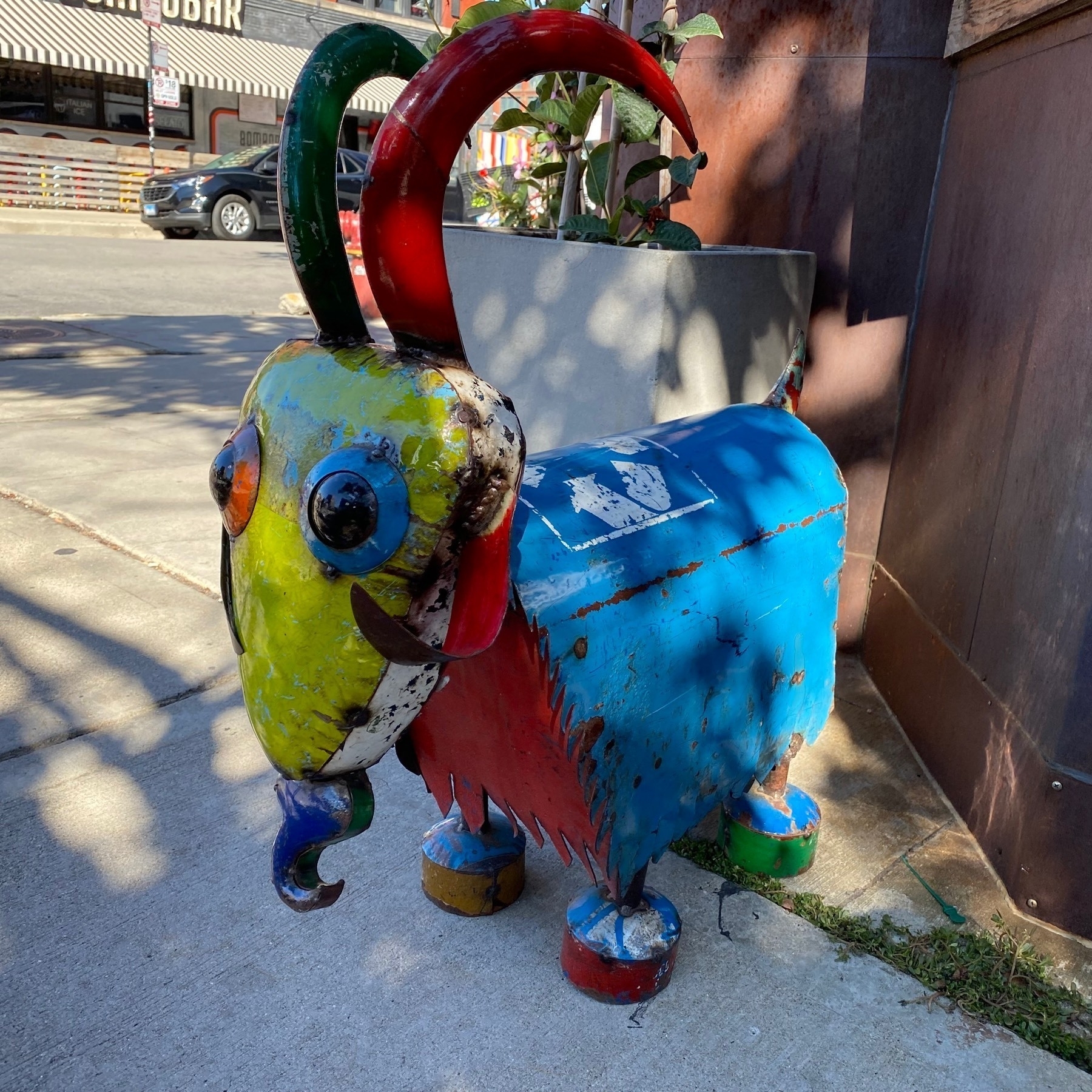 A colorful metal goat sculpture on the sidewalk.