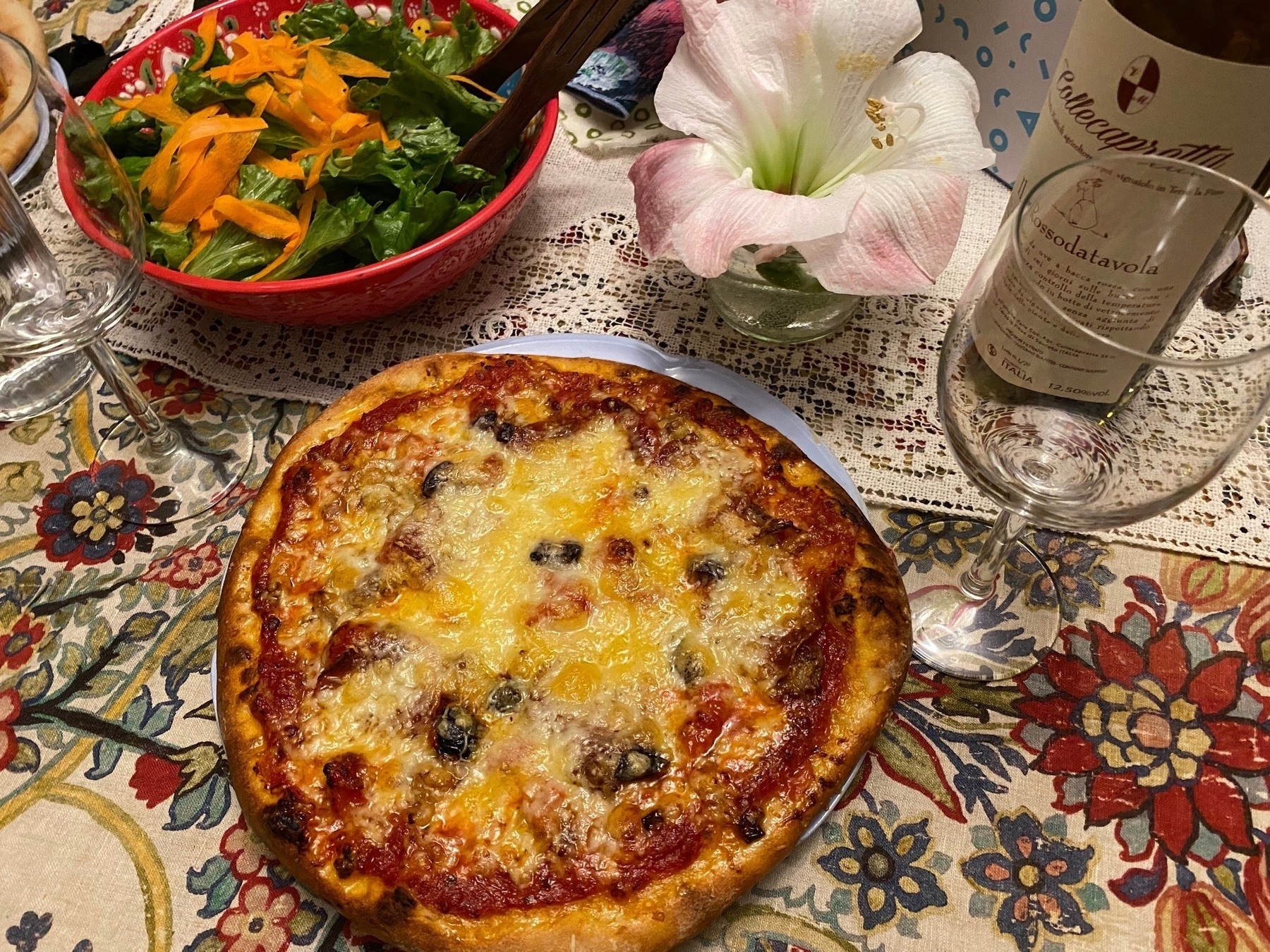 Small pizza on a table next to a salad and a wine glass.