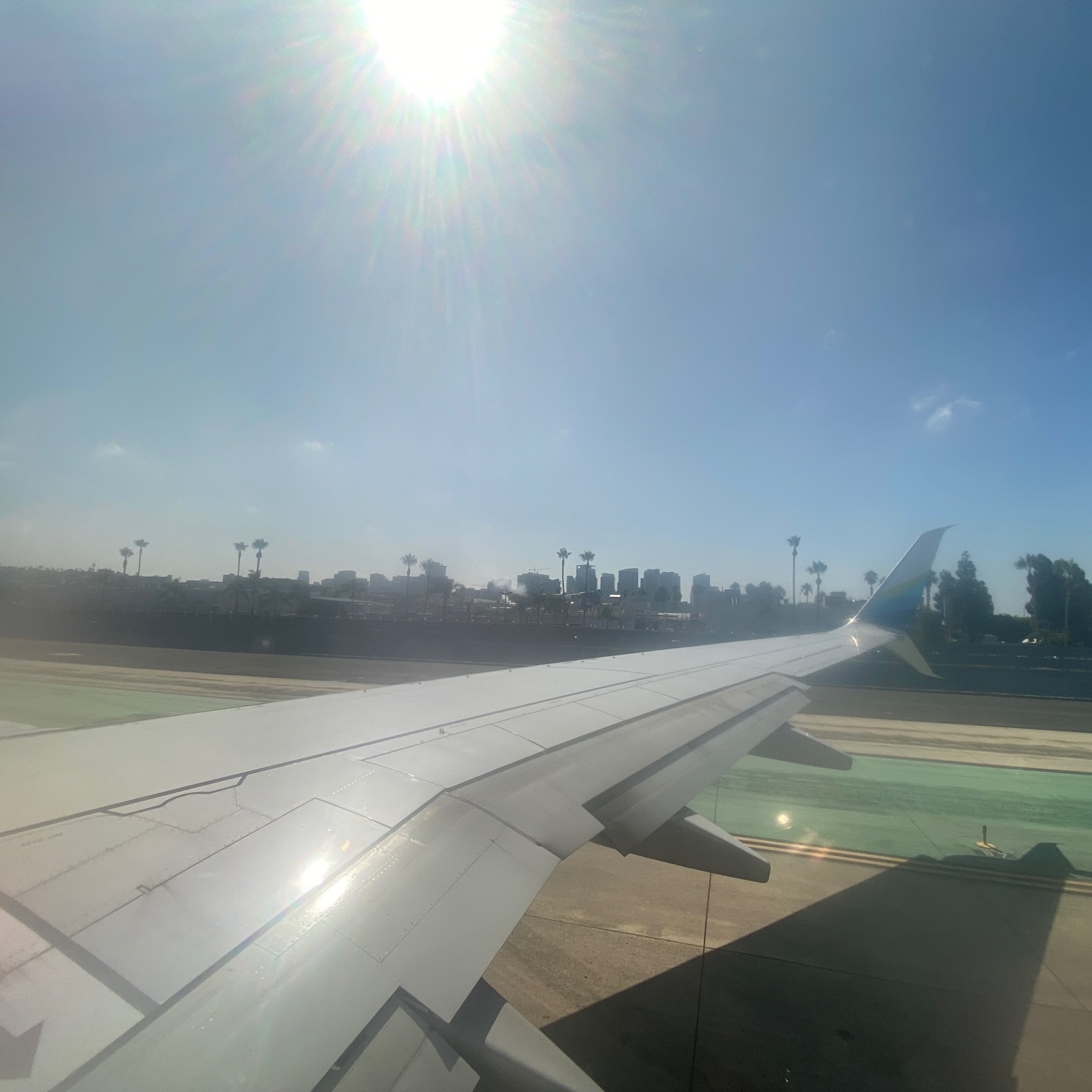 View out an airplane window on the taxiway with the bright sun above reflected off the wing below.