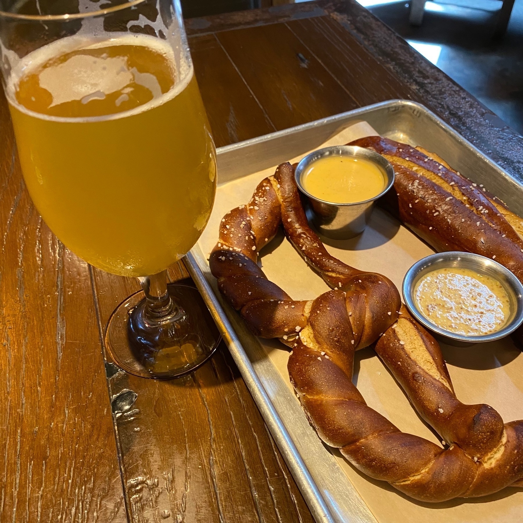 Glass of beer and a large pretzel on a wood table.