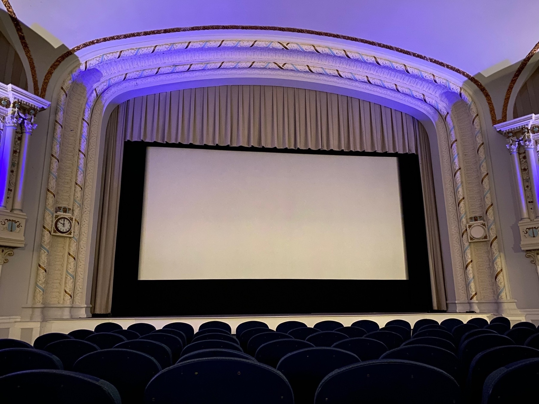 Empty movie theater with a blank white screen and purple side lighting.