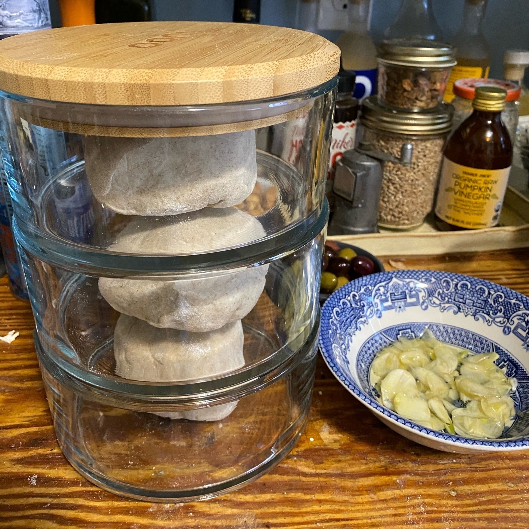 Stack of jars with dough balls sitting next to a small bowl of sliced garlic on a counter.