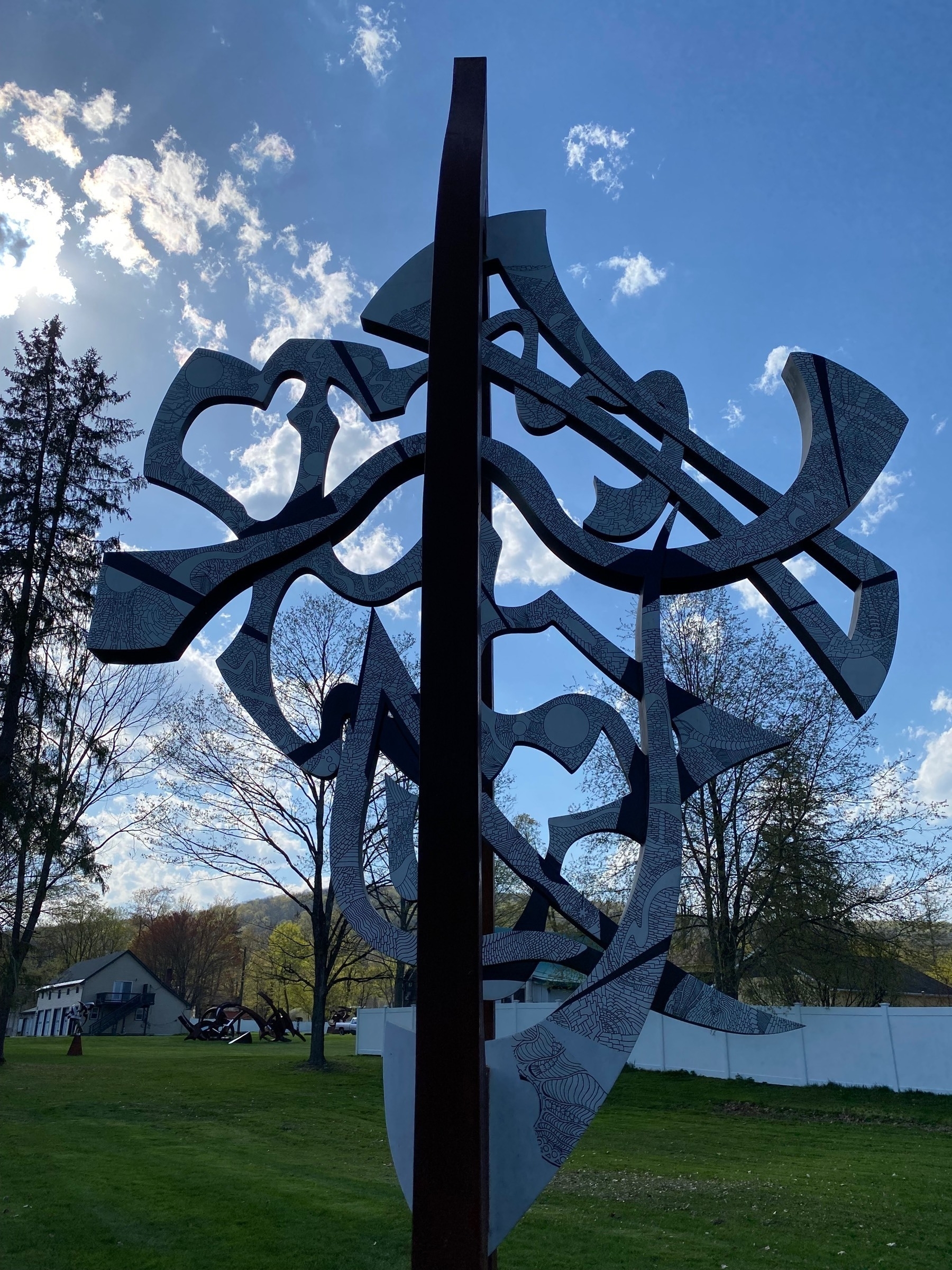 A metal sculpture against a blue sky with the sun behind clouds.