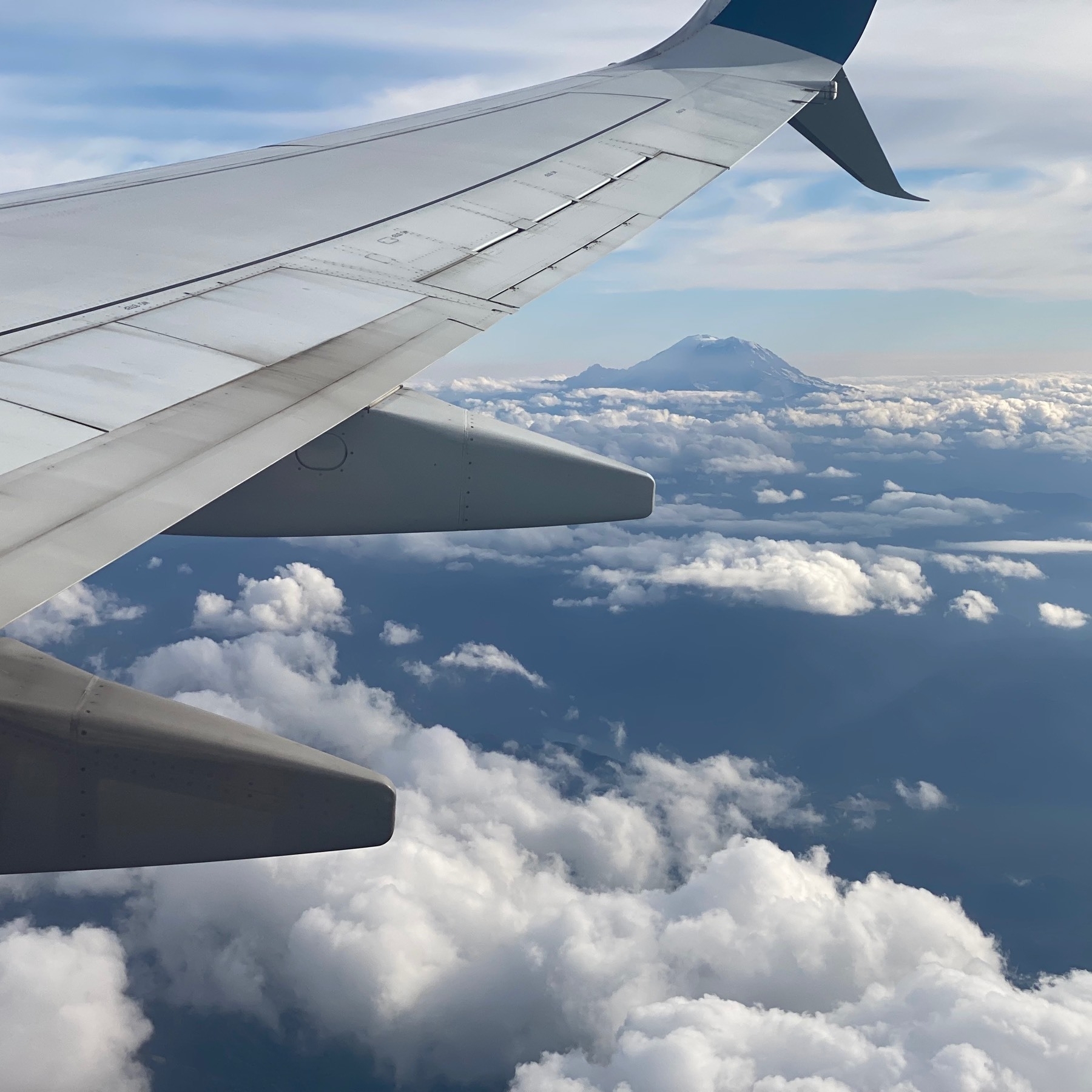 View from an airplane window of Mount Rainier on the horizon with the wing on the left. 