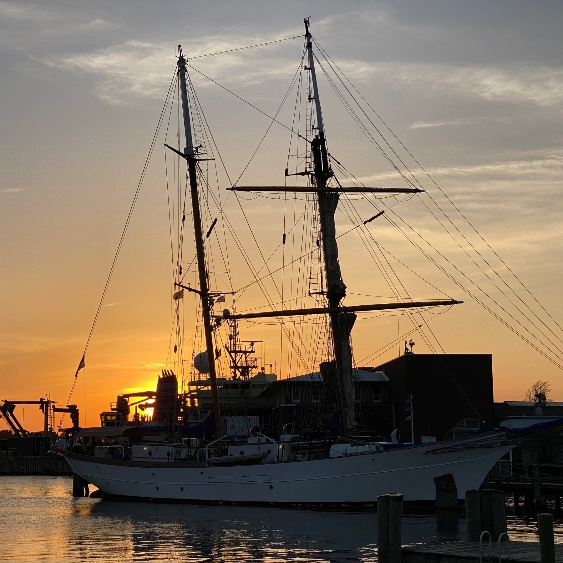 View at sunset of a harbor with a masted ship silhouetted against the sky.