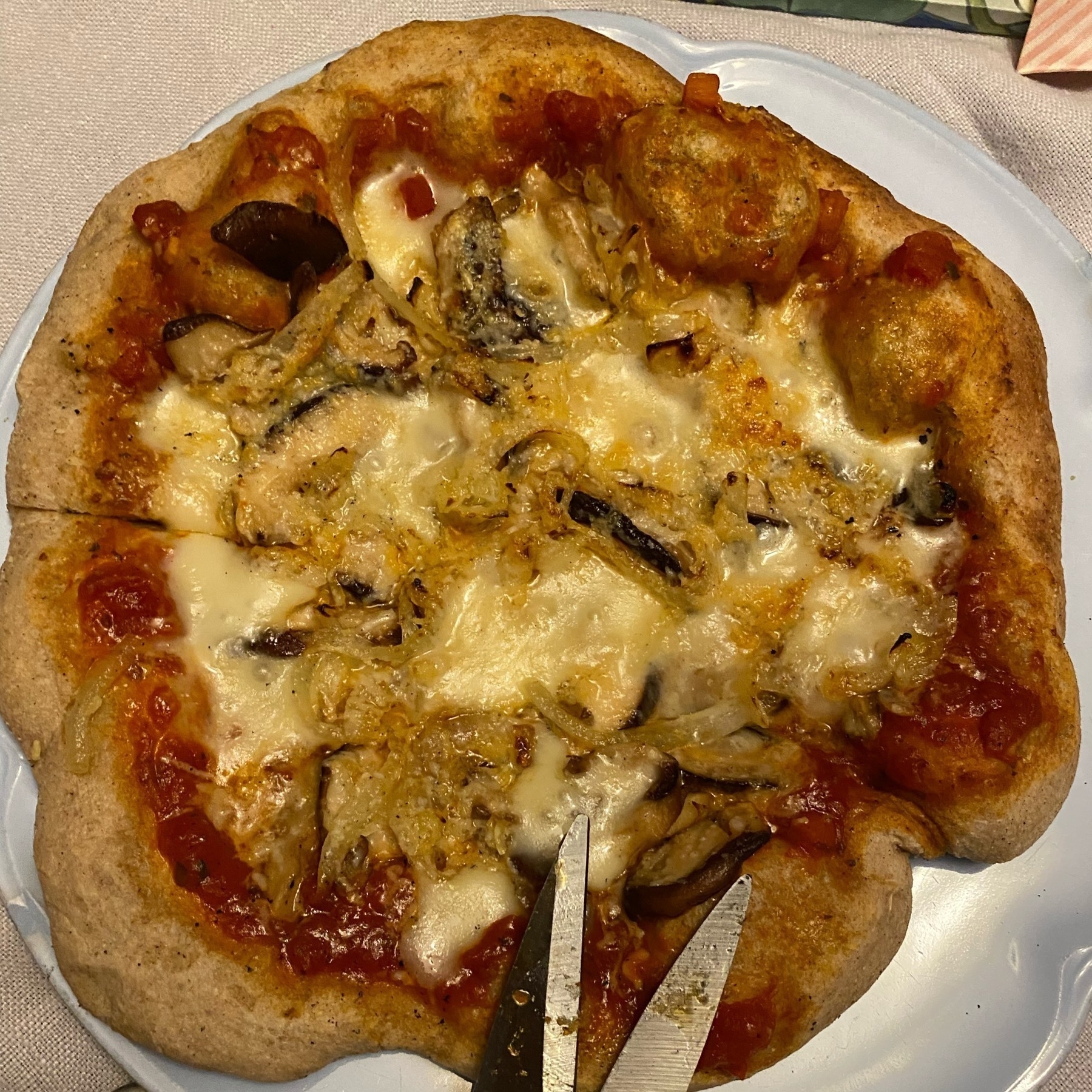 Small pizza on a plate with kitchen shears.