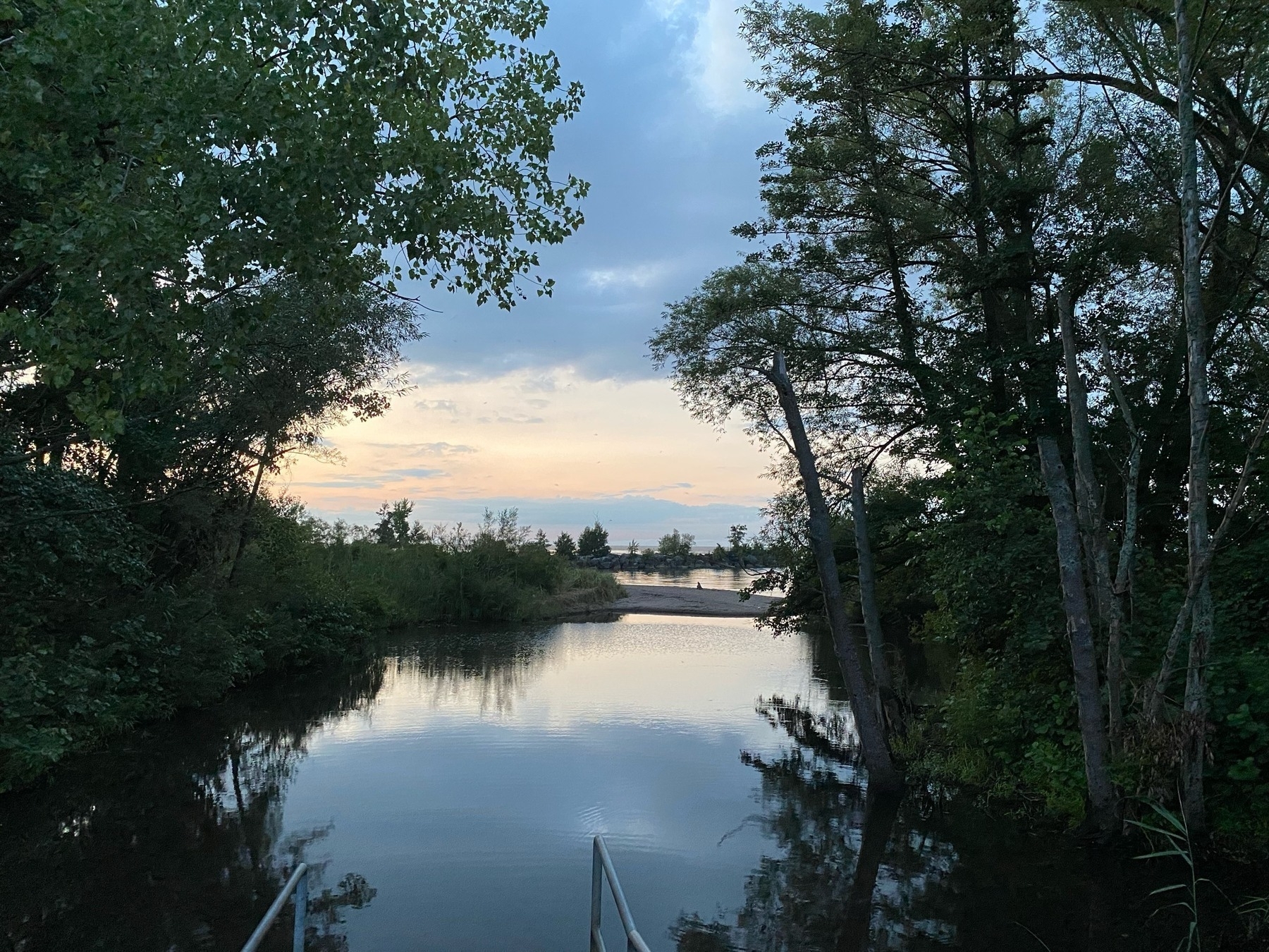 View of an inlet on a lake at twilight, framed by dark trees on either side.