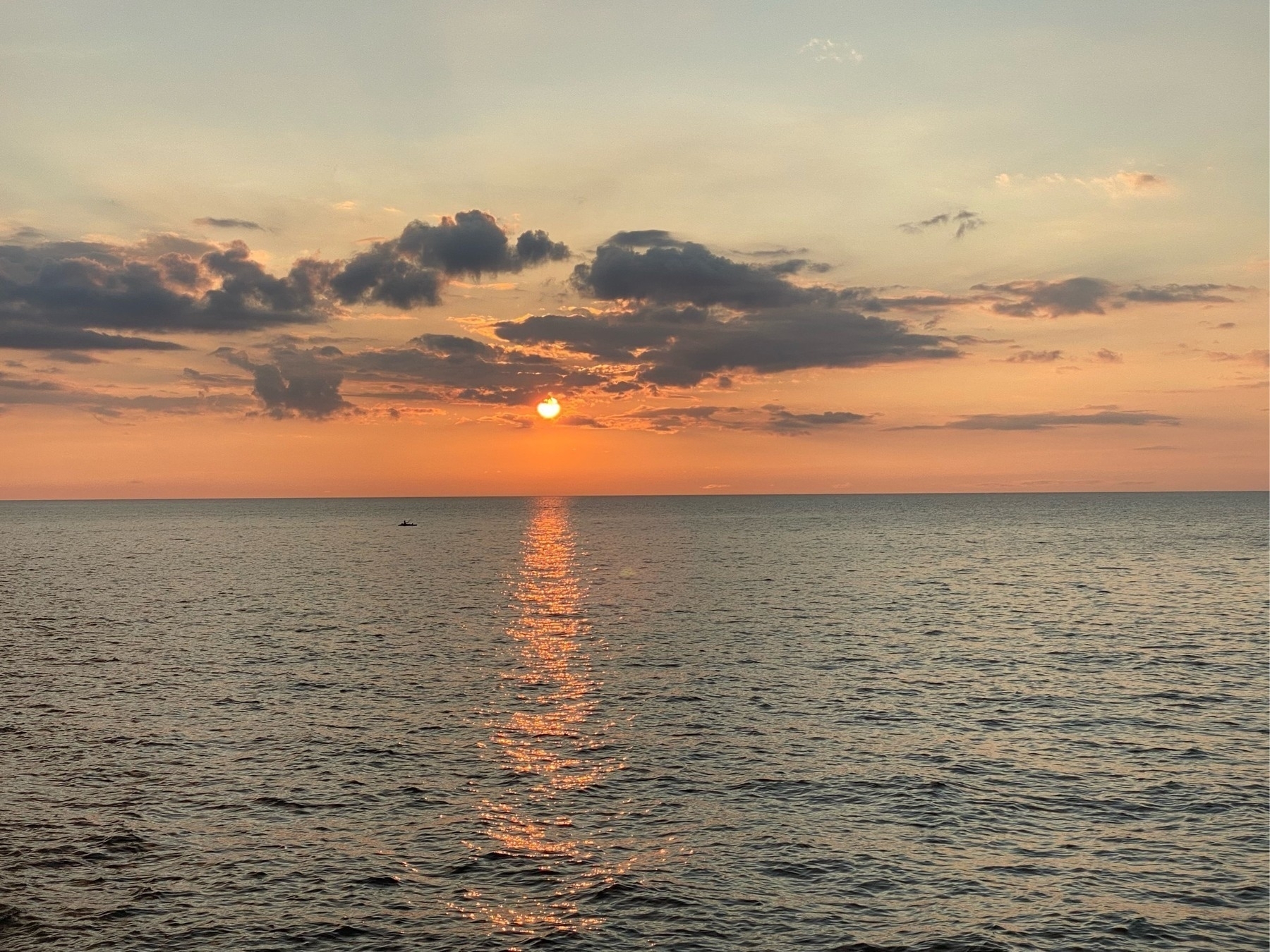 View of a sunset over a large lake, dark clouds along the horizon with orange light behind and the calm wares below. 